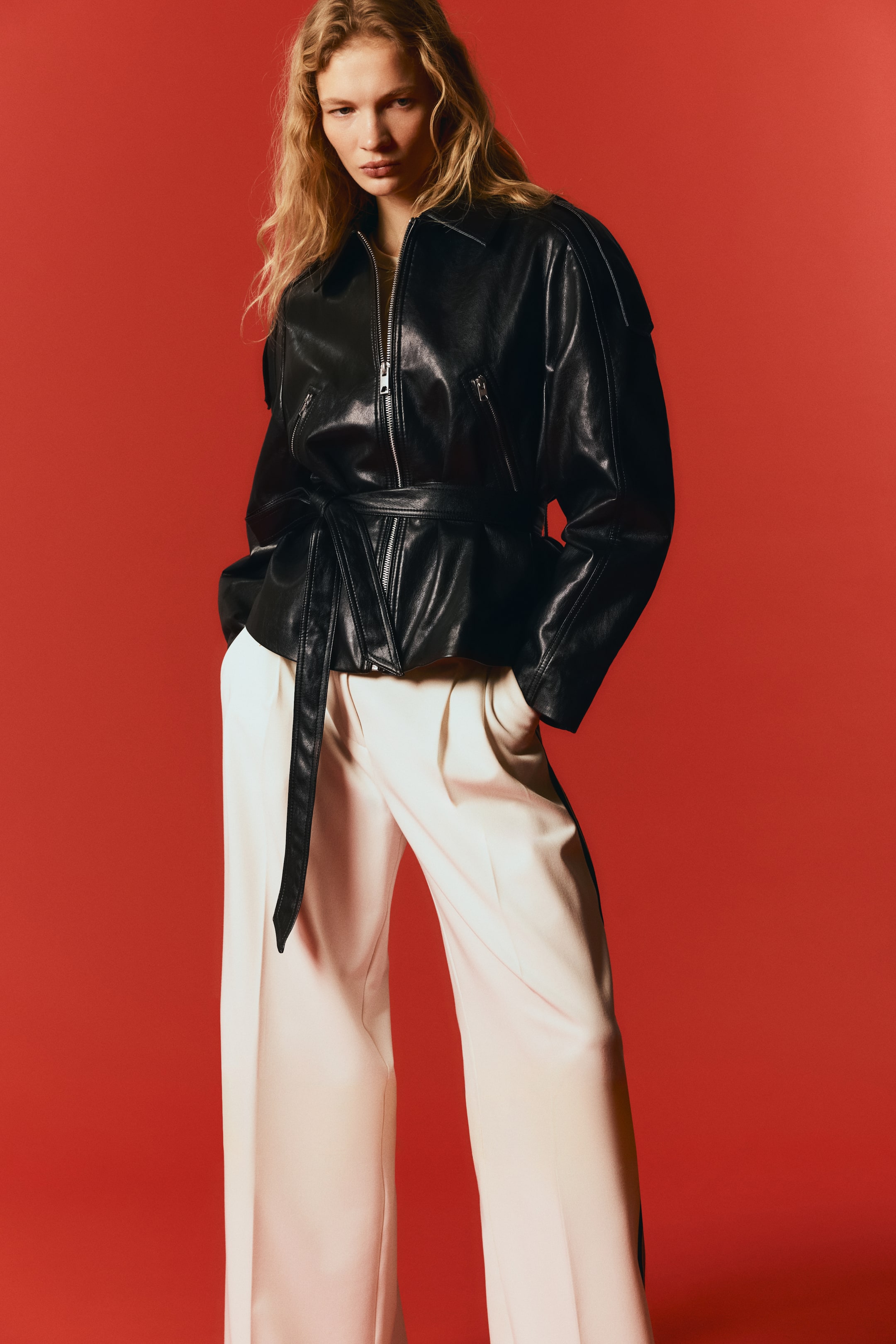 Zobacz większy obraz: Czarna kurtka z imitacji skóry z obniżonymi ramionami, zamkiem błyskawicznym z przodu, dwoma kieszeniami na piersi z zamkami oraz spiczastym kołnierzem. Dopasowany pasek do wiązania podkreśla talię.