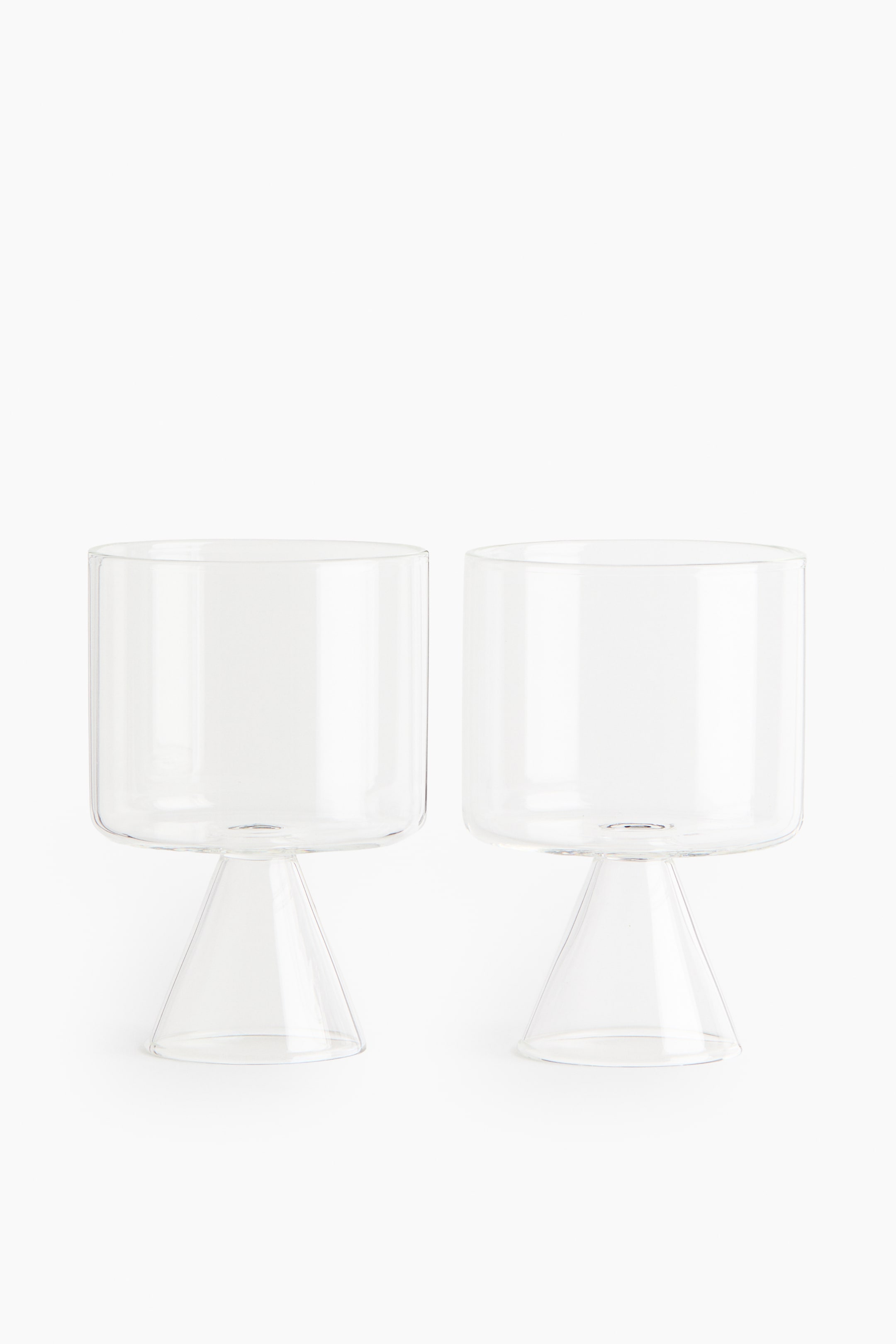 View larger image: Two borosilicate glass tumblers stand front and center, each showcasing a cylindrical top section gracefully perched on a sculptural, cone-shaped base.