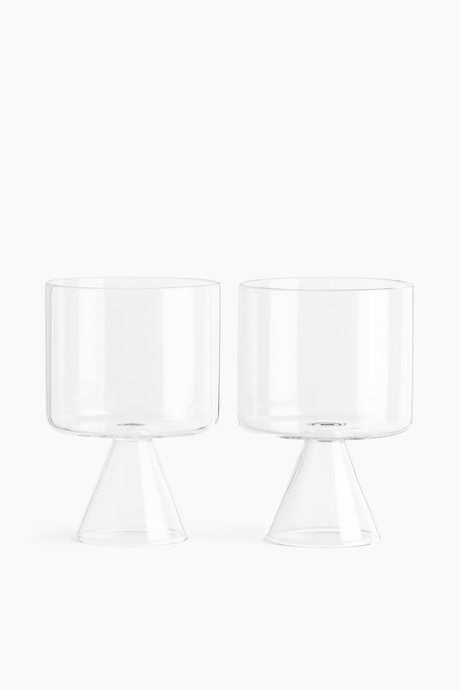 Deux gobelets en verre borosilicaté transparent, soufflés à la bouche, sont placés côte à côte, face à lâavant. Chaque gobelet présente une large coupe cylindrique reposant sur une base sculpturale creuse en forme de cône. - 1