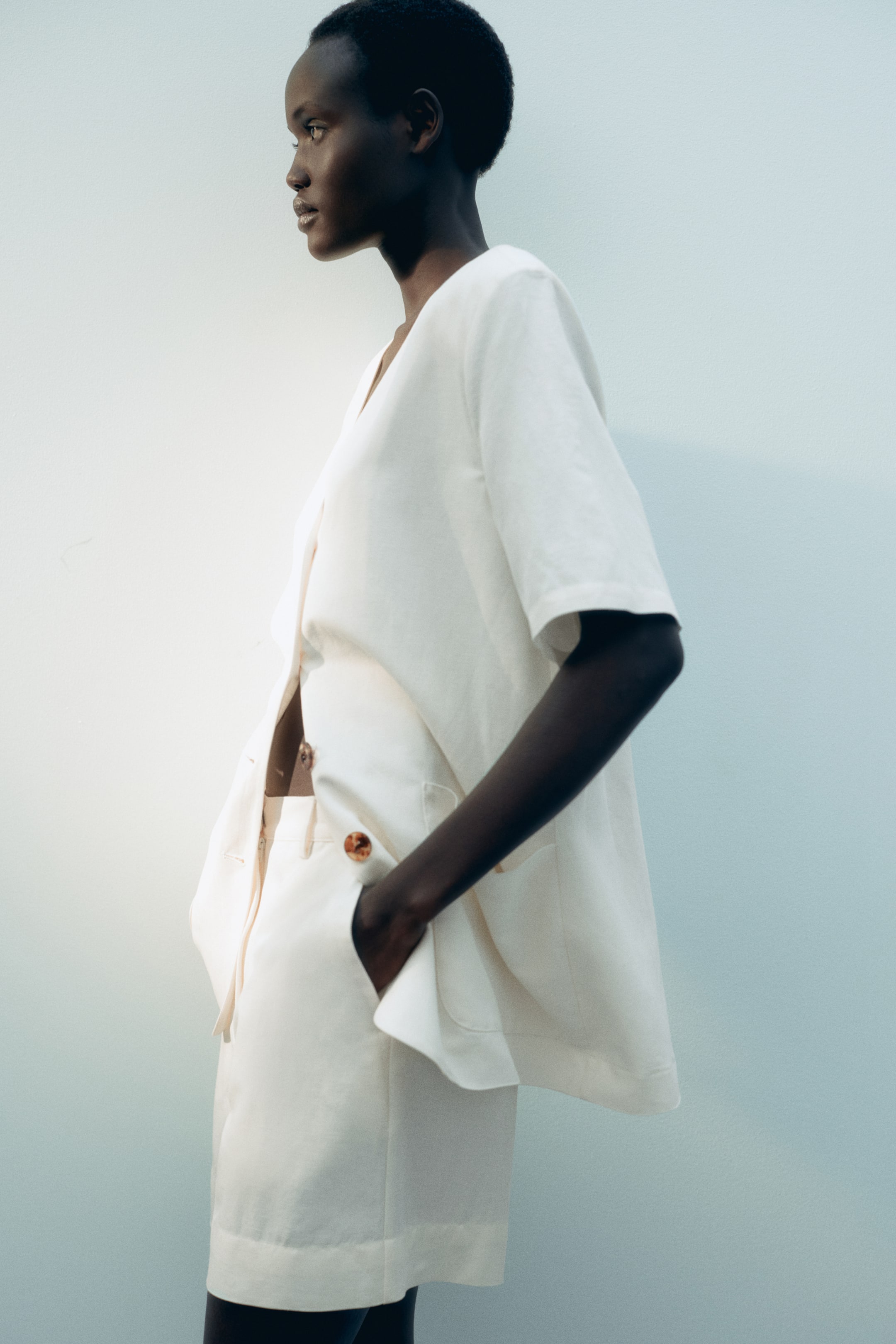 View larger image: The model is sporting light-coloured shorts crafted from a breezy linen blend. She stands with one hand casually placed in a diagonal side pocket.