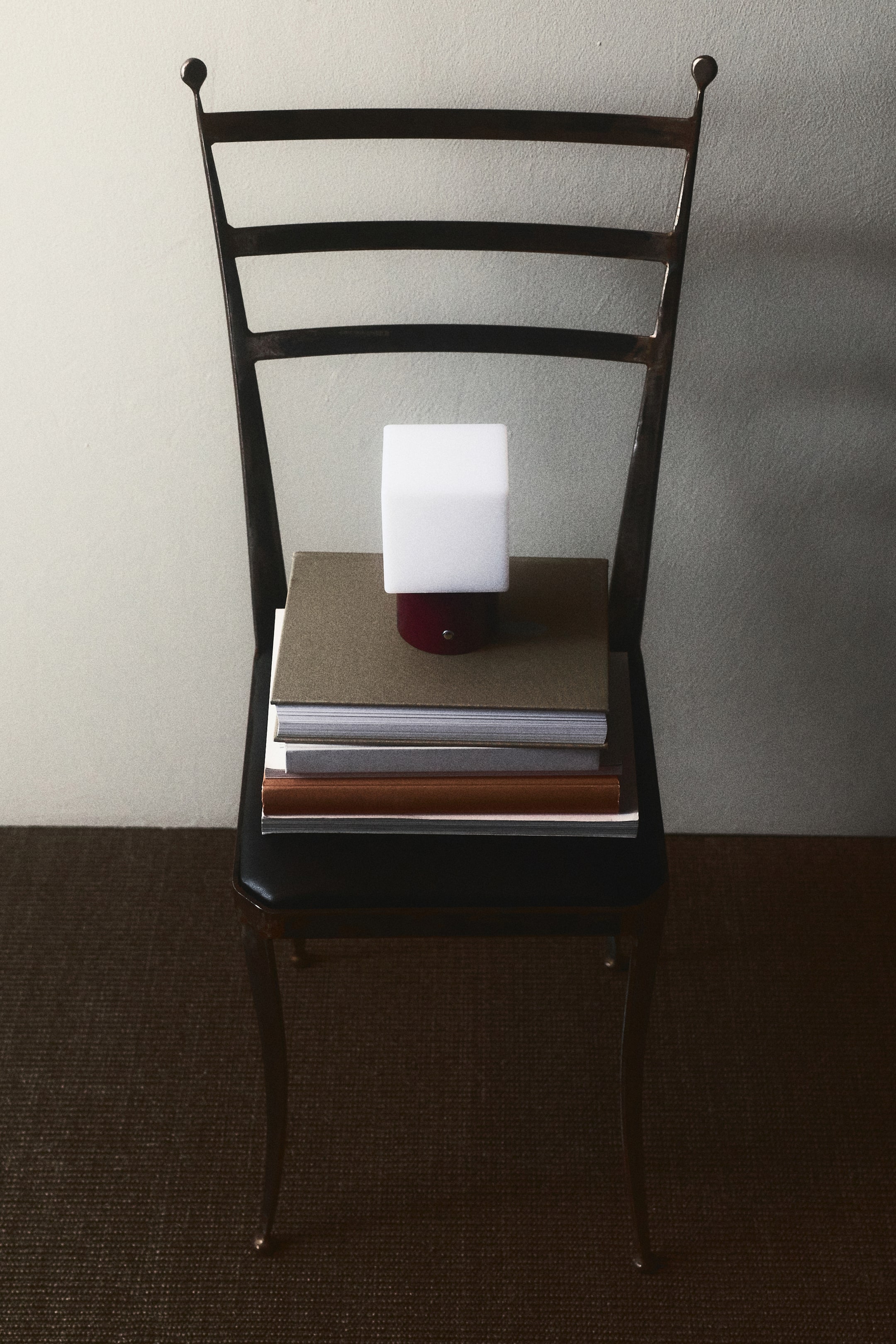 View larger image: Facing front, a rechargeable table lamp is displaying a cubic, translucent white plastic diffuser on top of a dark red cylindrical metal base with a small metallic button on the front.