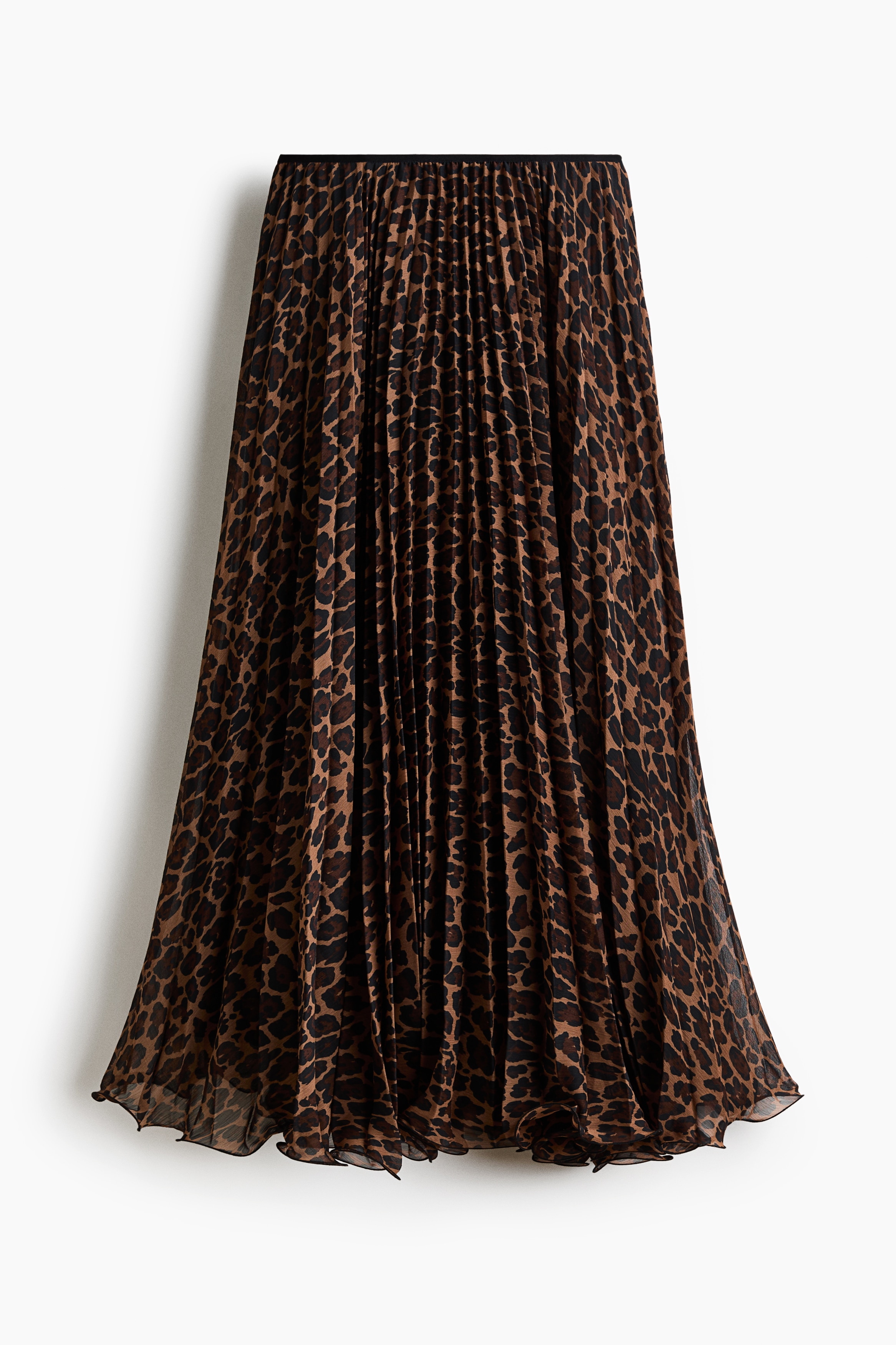 A leopard-print, pleated fabric skirt is being worn by the model while sitting. The loose-fitting skirt is styled with a long-sleeved black knitted sweater.