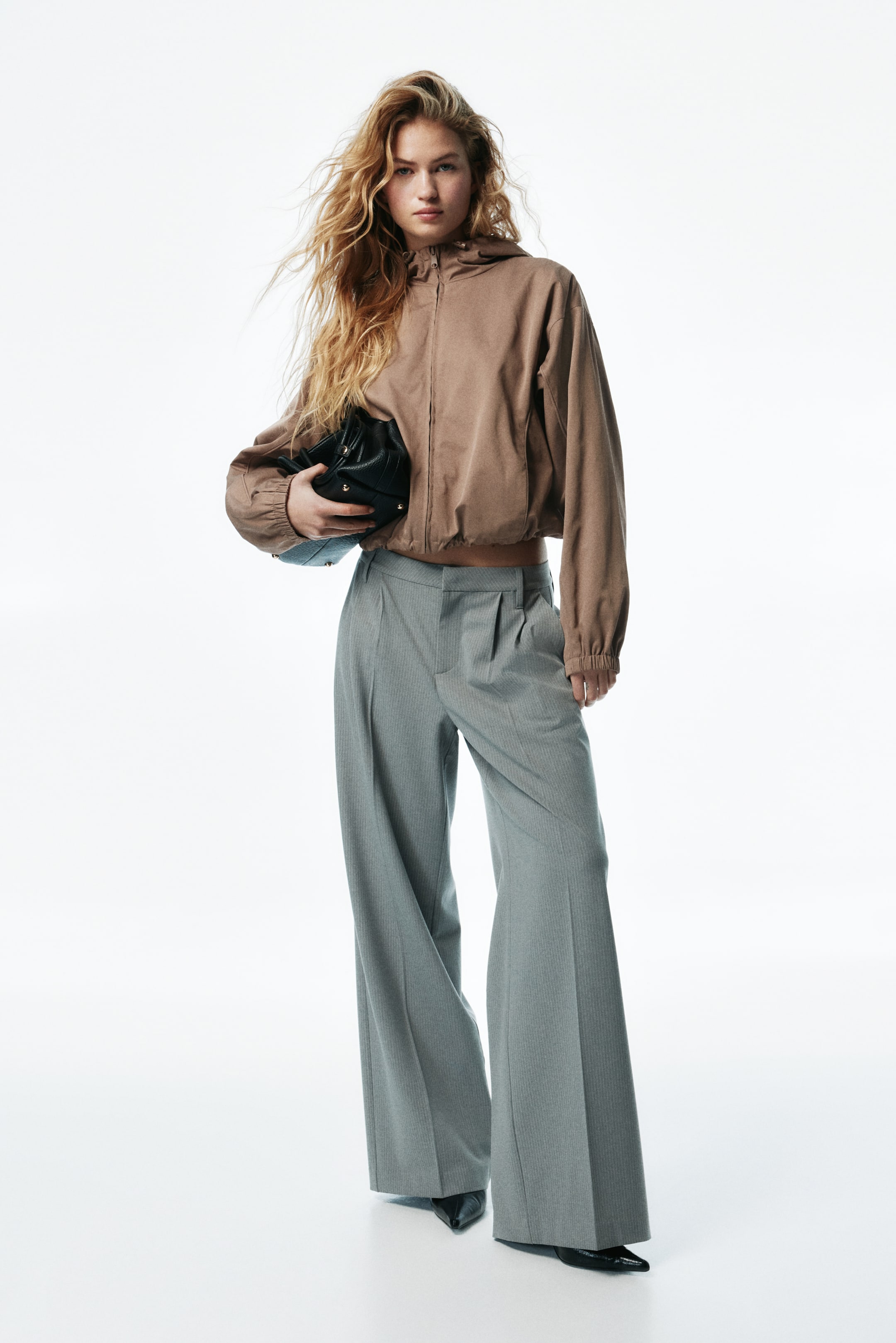 View larger image: Grey pleated wide-leg pants are featuring a subtle vertical stripe pattern and pleats at the front. The pants are presenting a loose, flowing fit from the waist, extending to the floor.