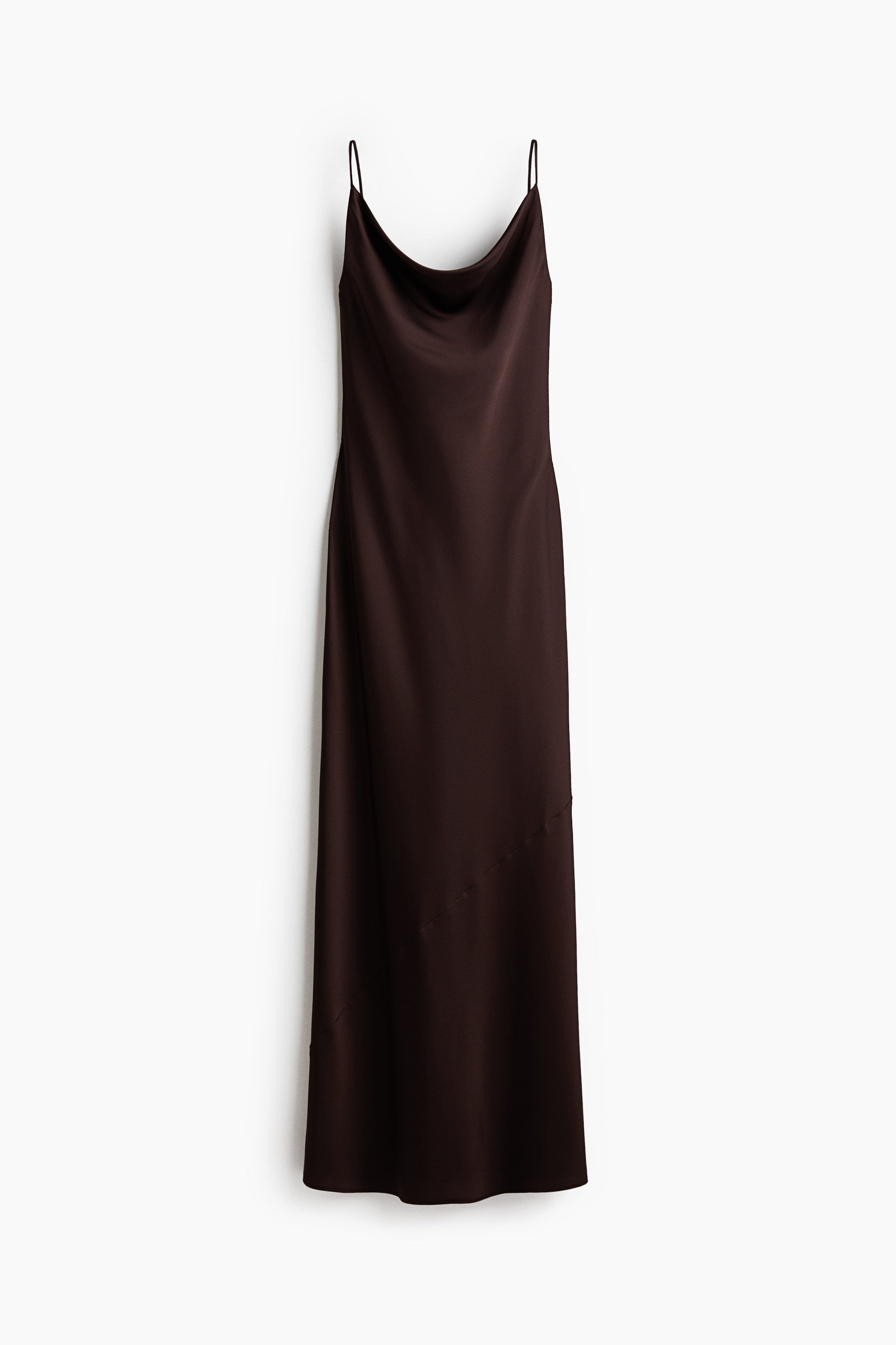 The model is wearing an ankle-length fitted dark brown satin dress with a cowl neckline and slender spaghetti straps. She is holding a small black clutch bag with long fringe detailing.