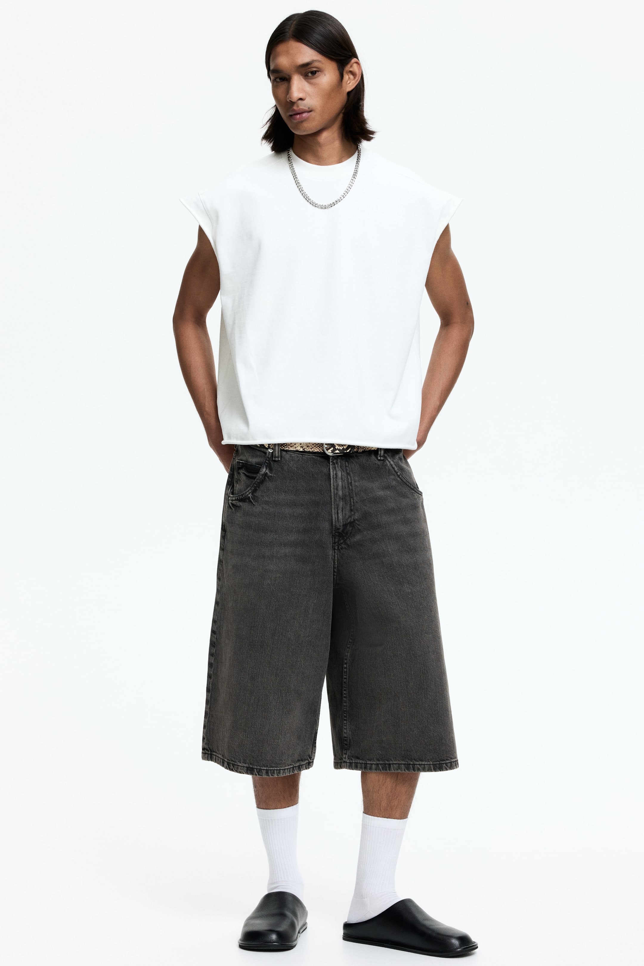 View larger image: Dark grey denim shorts feature a wide-leg, knee-length cut with a faded wash and frayed hems. They show distressed details near the front pockets, and a patterned belt is visible in the waistband.