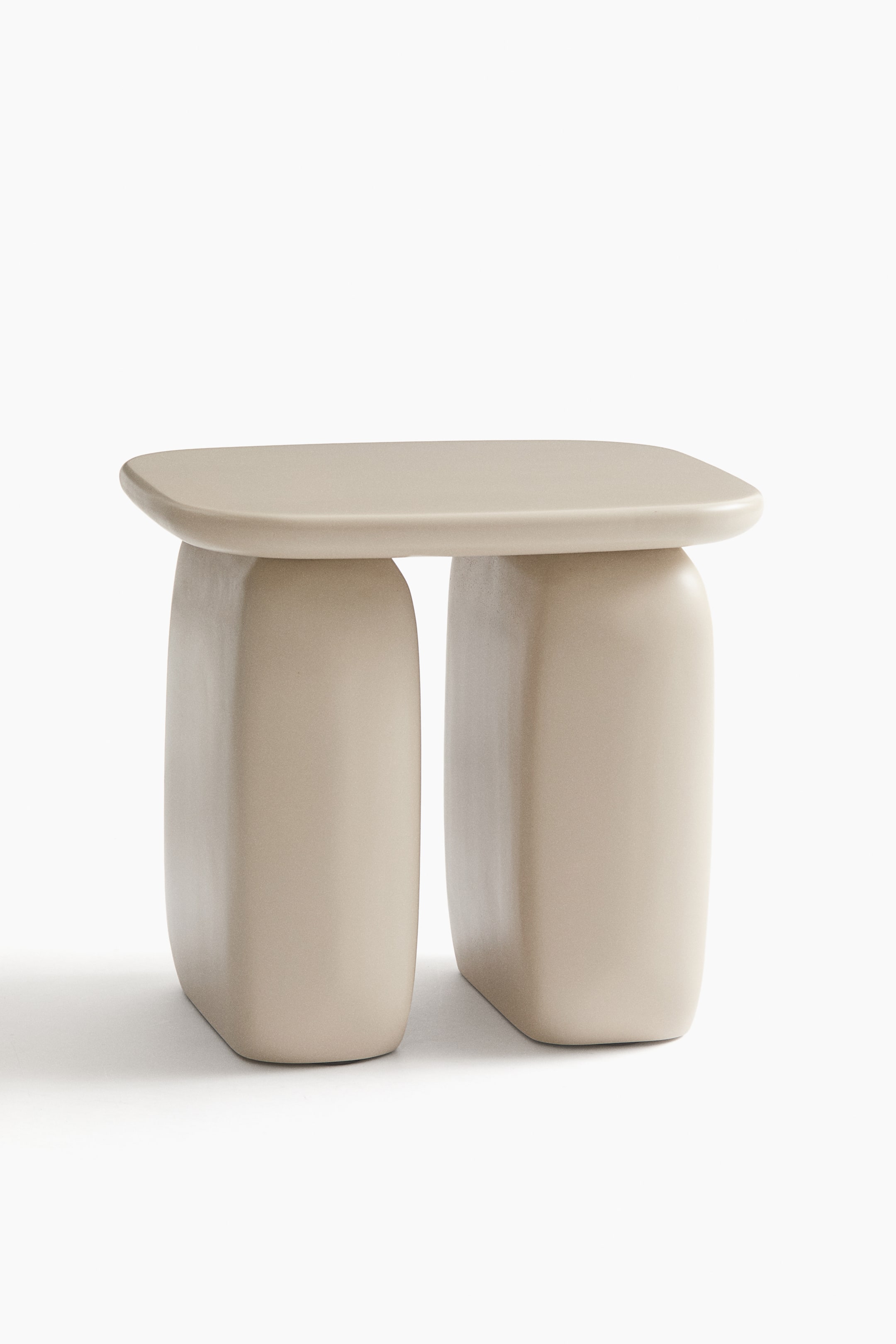 Grotere afbeelding bekijken: Een lichtbeige tafel met een rechthoekig blad met zacht afgeronde hoeken, ondersteund door twee stevige, afgeronde blokvormige poten die uit elkaar staan, alles met een gladde, matte afwerking.