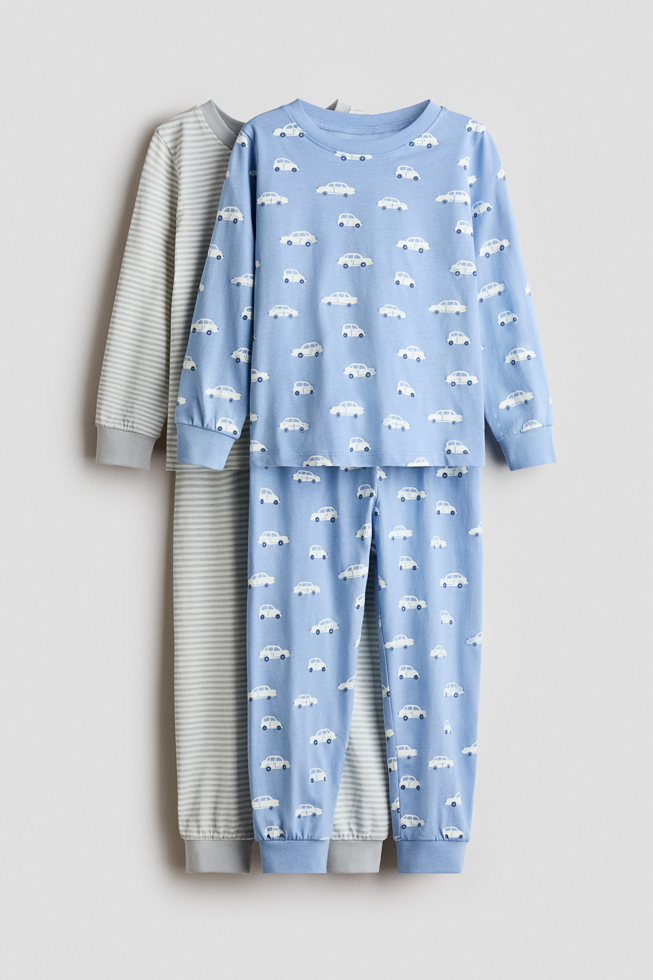 View larger image: A light blue pair of pyjamas is shown from the front, featuring an all-over white car print. The long-sleeved top includes a round, rib-trimmed neckline and ribbed cuffs, while the bottoms have an elasticated waist and ribbed hems.