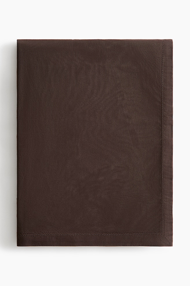 A folded dark brown cotton tablecloth displays its fine woven texture and a delicate hemstitched border running parallel to the wide hemmed edges. The tablecloth is presented from a flat-lay perspective, showcasing its clean rectangular shape and neat finish. - 1