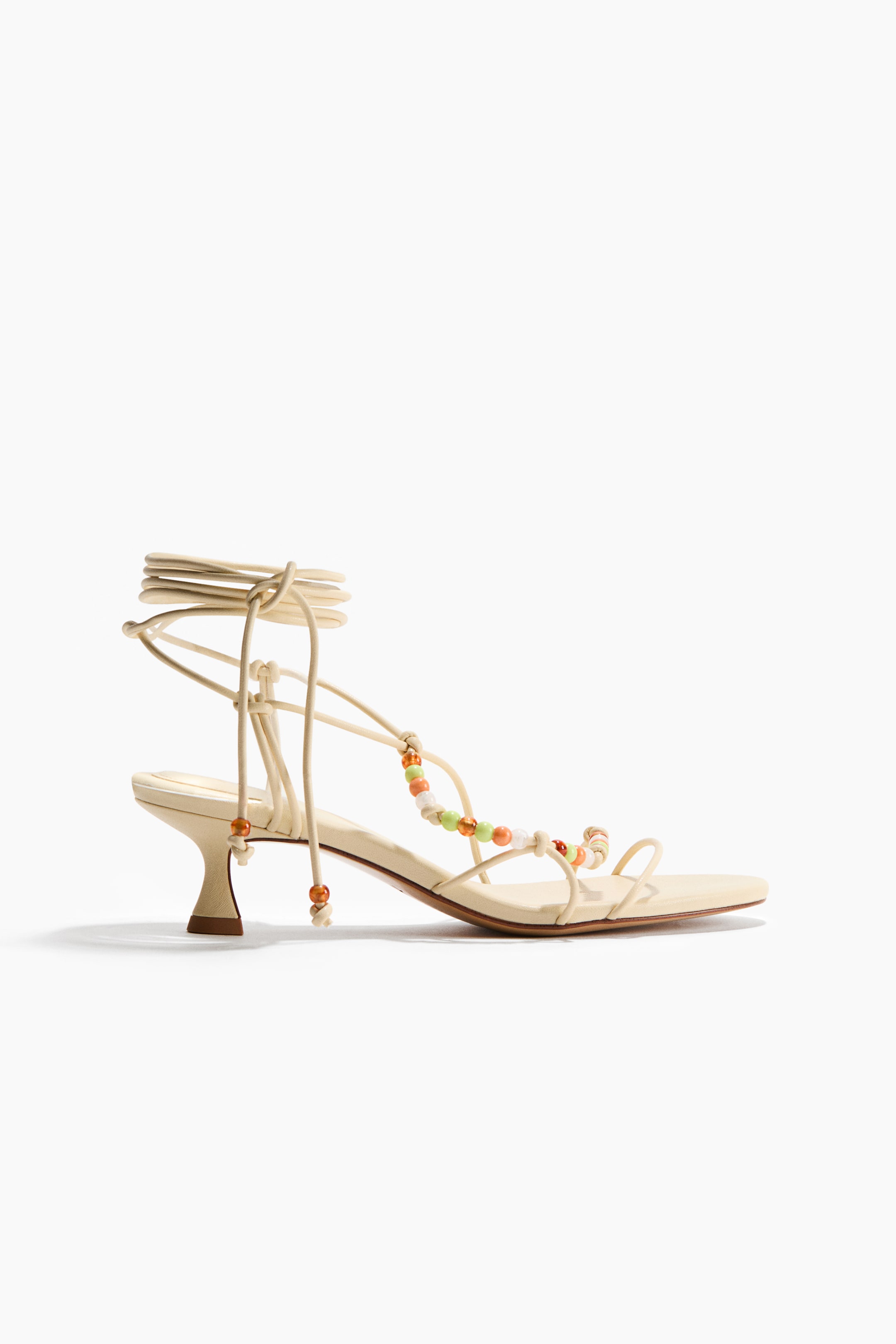 View larger image: Sandals showcase a coated fabric with knotted spaghetti foot straps adorned with vibrant plastic beads. Extended spaghetti ties elegantly wrap around the ankle, and the sandals feature almond toes and flared kitten heels.