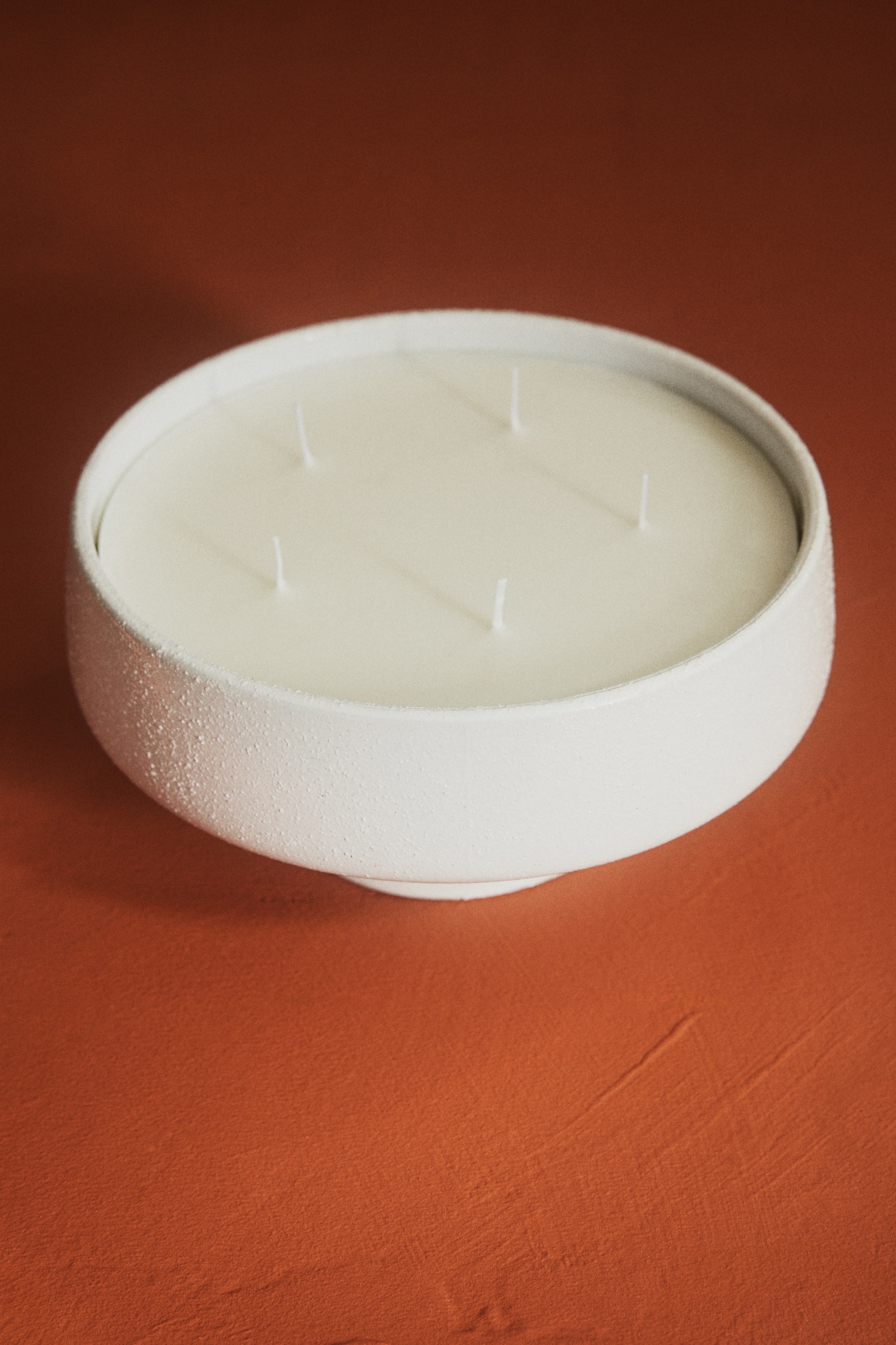Visualizza immagine più grande: Una candela extra-large a cinque stoppini è presentata in un portacandela in gres bianco con texture, caratterizzato da una forma a ciotola ampia con un piede sottile e una superficie di cera liscia color crema chiaro.