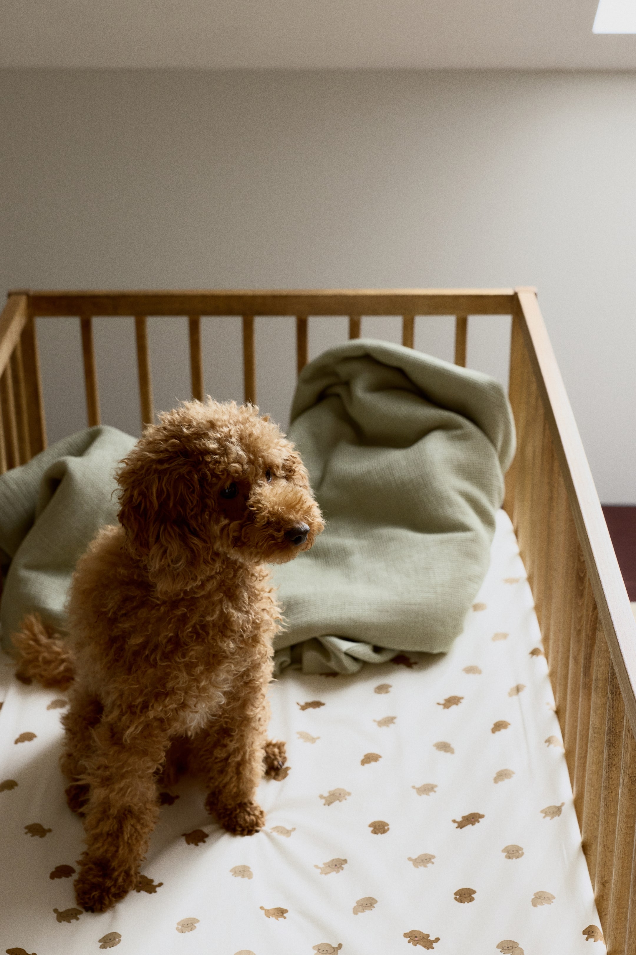View larger image: A cream-colored crib sheet covers the mattress, showcasing a pattern of small, repeated light brown and medium brown puppy illustrations.