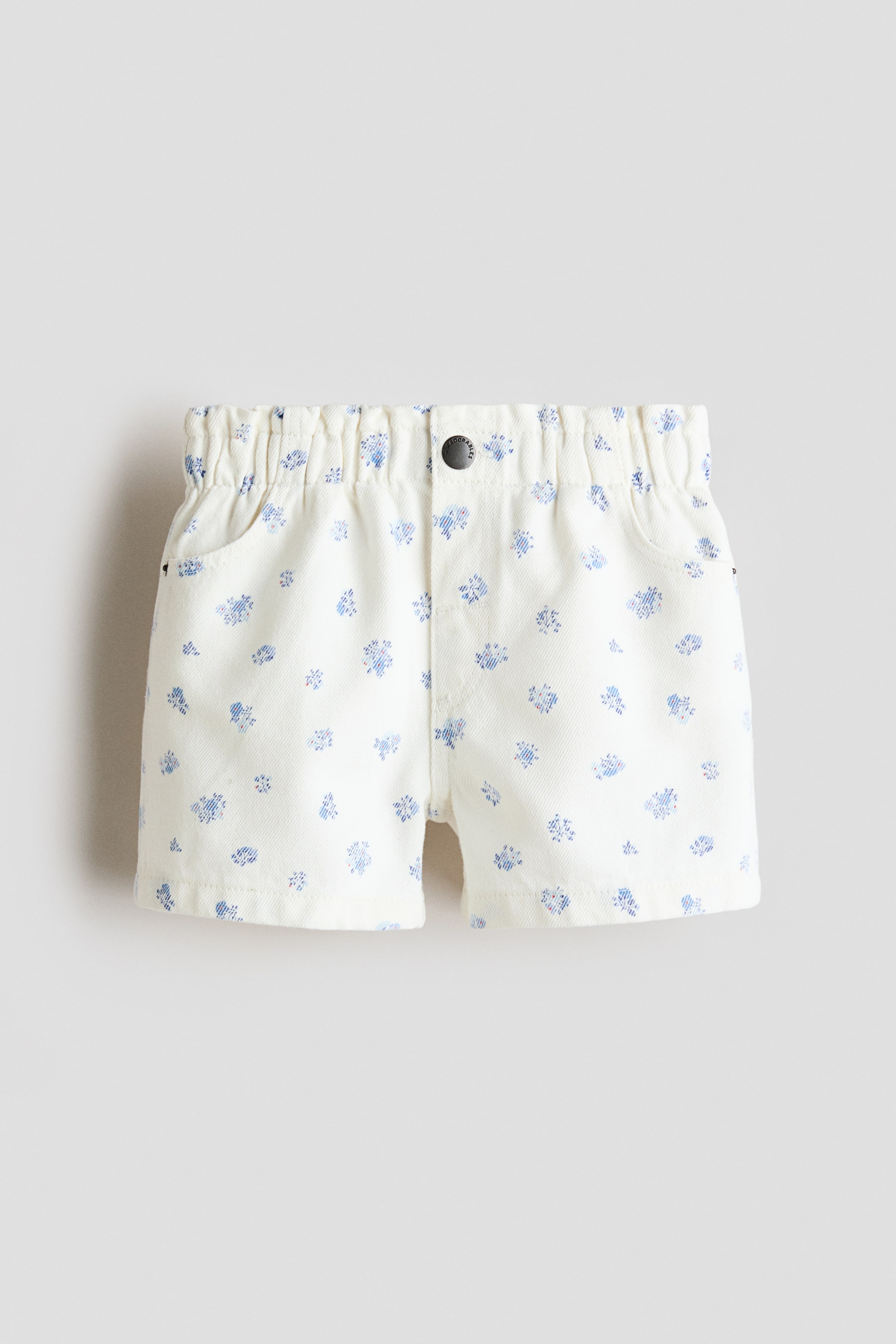 View larger image: These off-white shorts, showcased from the front, boast blue floral patterns, an elasticated waistband, a single dark button closure, and two side pockets.