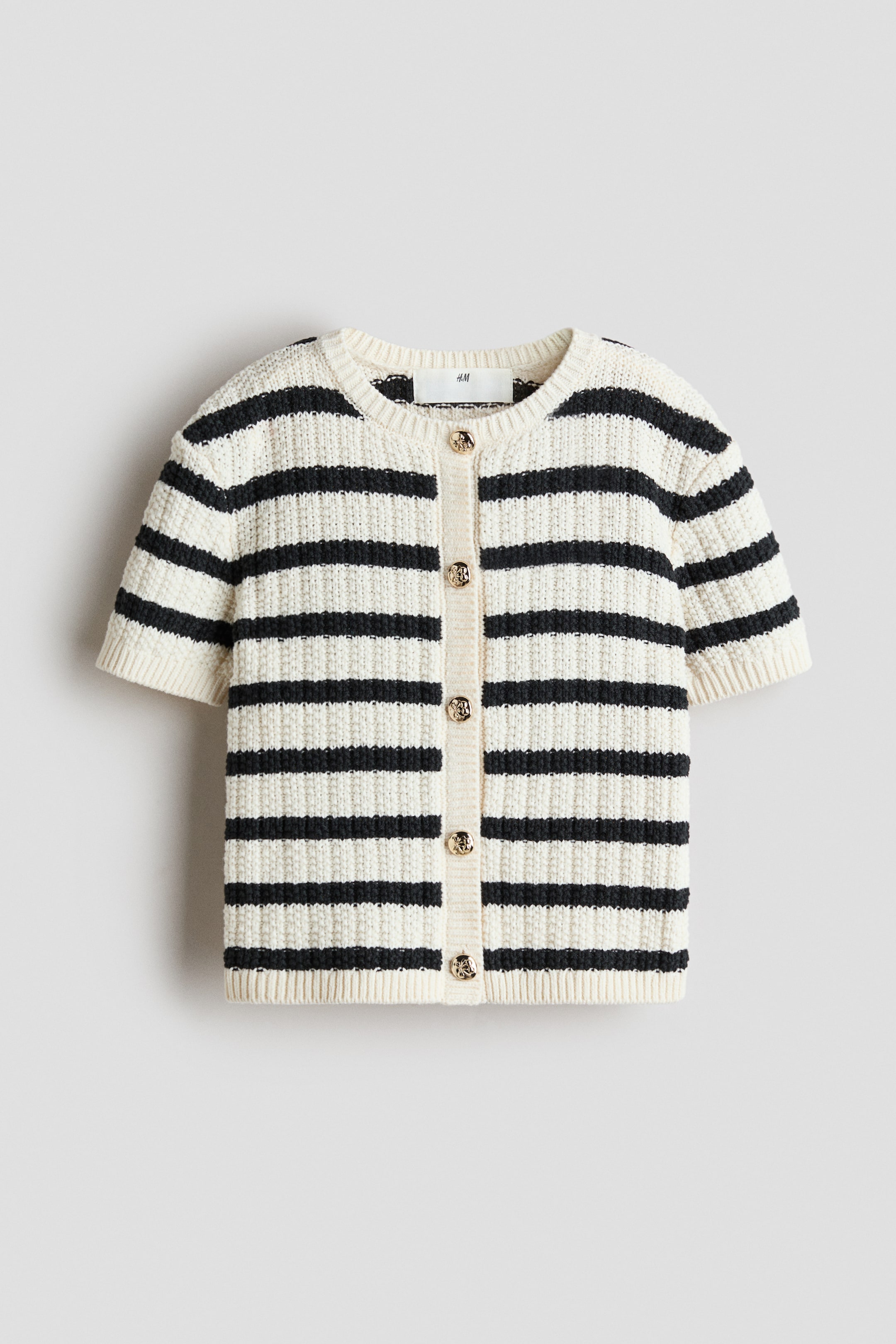 View larger image: This short-sleeved cardigan showcases a cream-hued textured knit adorned with black horizontal stripes, displayed in a front-facing manner. It boasts a crew neck, ribbed short sleeves, and a ribbed hem, fastening down the front with round, gold-toned buttons.