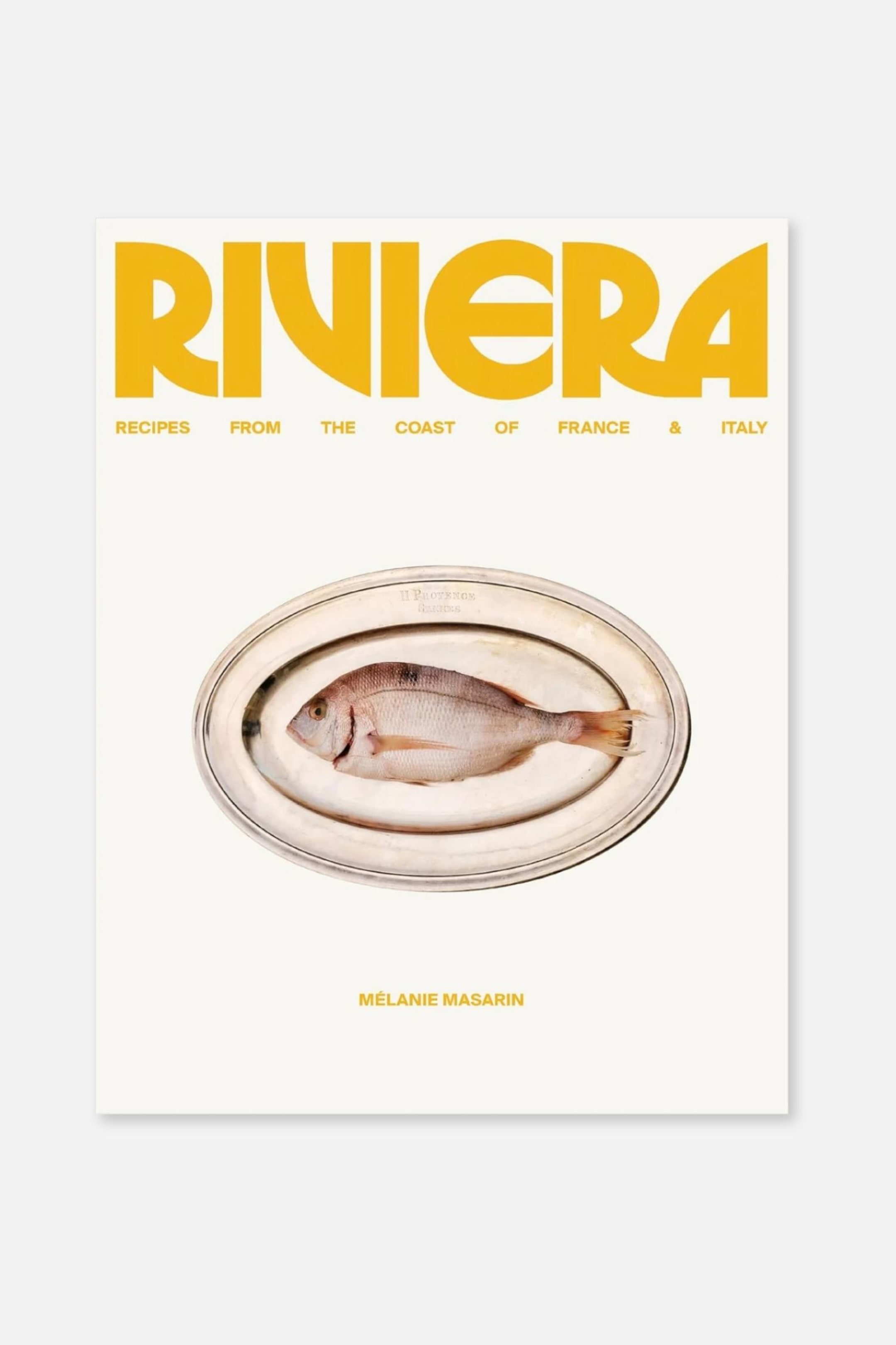 Größeres Bild ansehen: Eine frontal ausgerichtete Kochbuchcover-Gestaltung zeigt den Titel „RIVIERA“ in kräftiger gelber Schrift über dem Untertitel „RECIPES FROM THE COAST OF FRANCE & ITALY“ auf cremeweißem Hintergrund. In der Mitte befindet sich ein Bild eines ganzen rohen Fisches, der auf einer ovalen silbernen Platte liegt, während der Name der Autorin „M�LANIE MASARIN“ unten in Gelb erscheint.