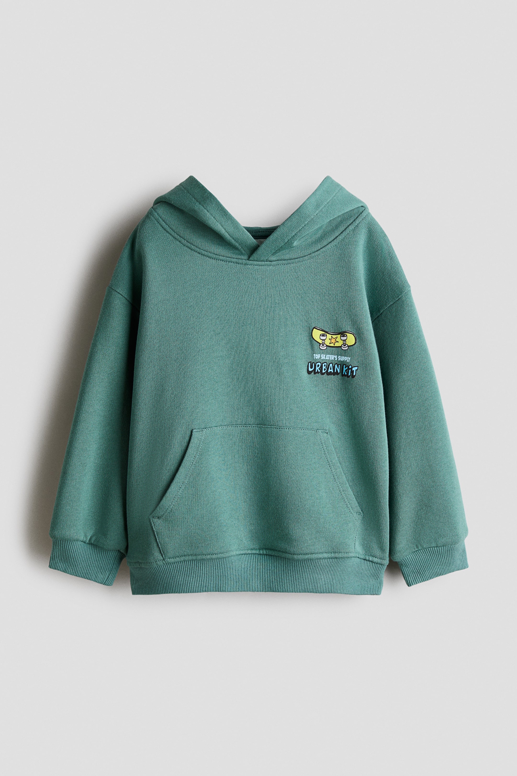 View larger image: A relaxed-fit green hoodie is shown from the front, featuring a wrap-front hood, dropped shoulders, and a front kangaroo pocket. A small yellow skateboard graphic with the text "URBAN KIT" is printed on the left chest, with wide ribbed trims finishing the cuffs and hem.