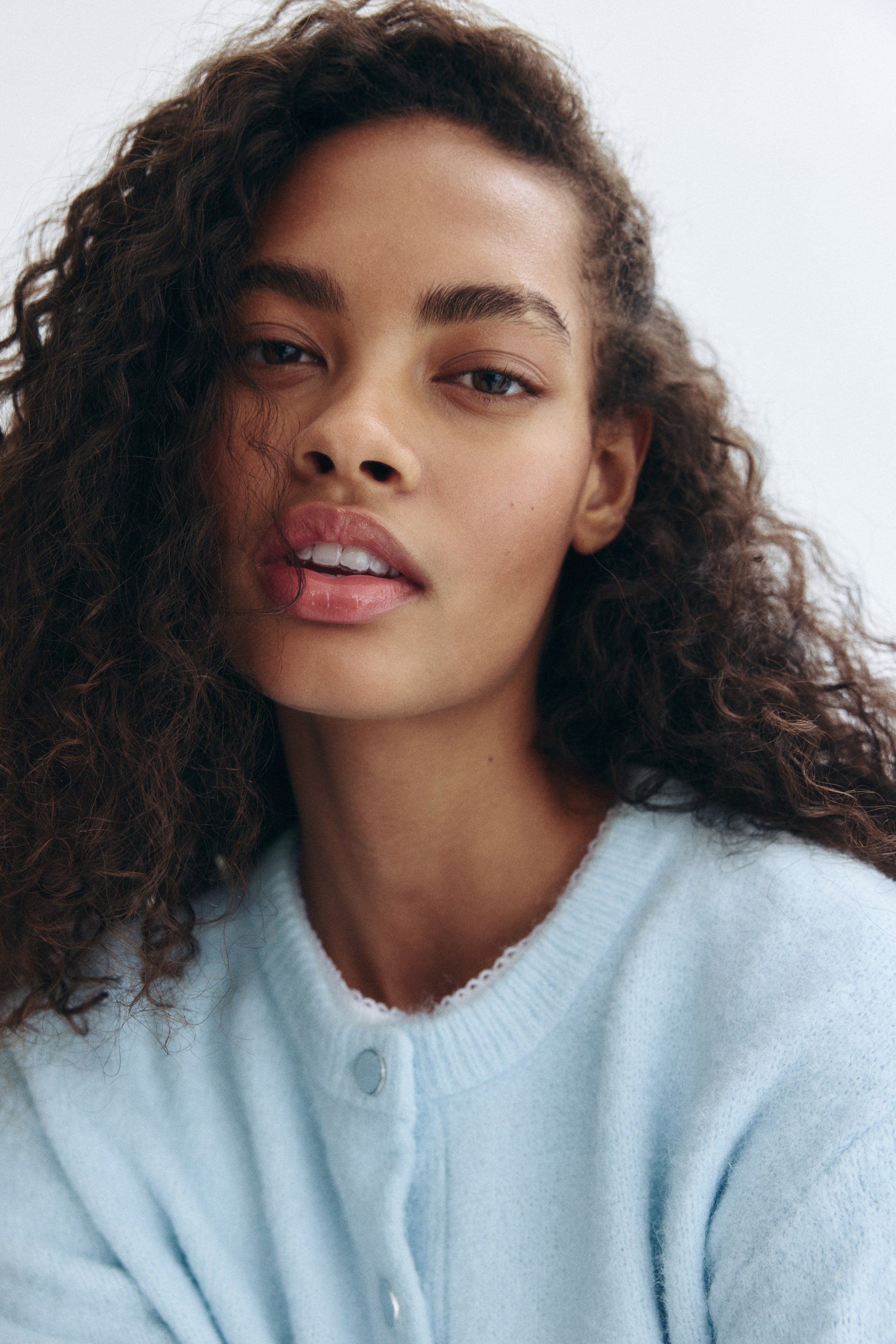 Visualizza immagine più grande: Un cardigan lavorato a maglia di colore azzurro è indossato dalla modella. Presenta uno scollo rotondo con una chiusura a bottoni di colore argento visibile, e un delicato bordo bianco appare da sotto il colletto.