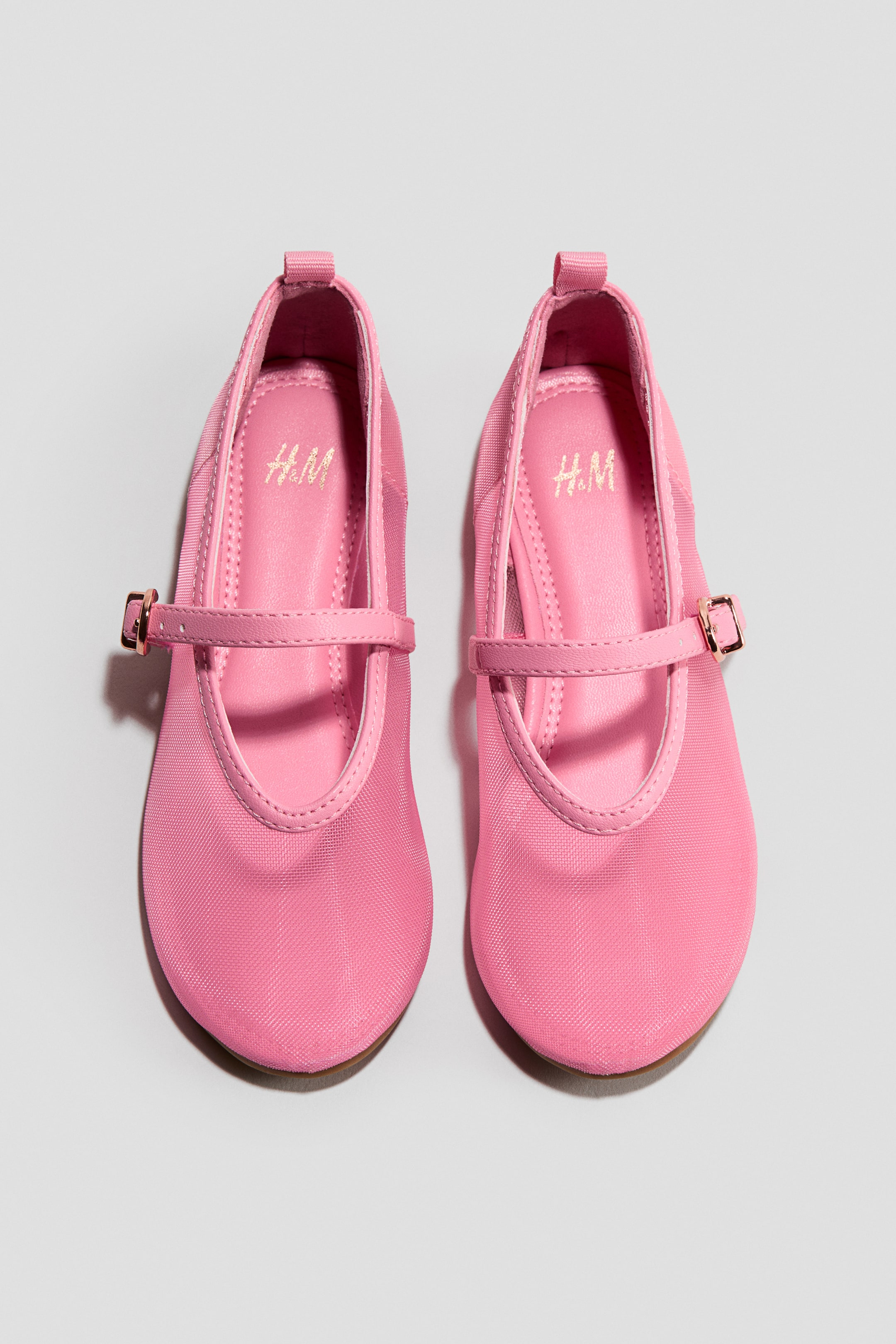 הצגת תמונה גדולה יותר: זוג נעלי בלרינה מרי ג'יין בטקסטיל ורוד ממוקמות מקדימה, מציגות קצה מעוגל ורצועה על פני הקשת. כל רצועה כוללת אבזם קטן בצבע זהב והסוליה הפנימית המרופדת מציגה לוגו זהוב H.M.