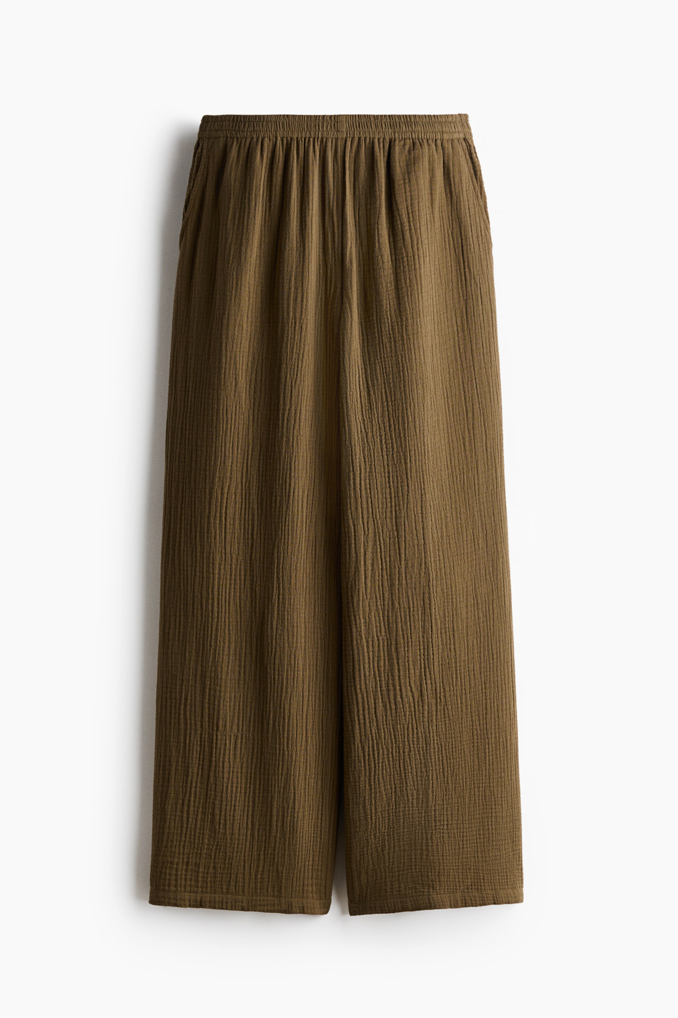 View larger image: "The olive green trousers are showcasing a front view, highlighting an elasticated waist that gathers the soft, crinkled cotton muslin fabric. They feature diagonal side pockets and straight legs."