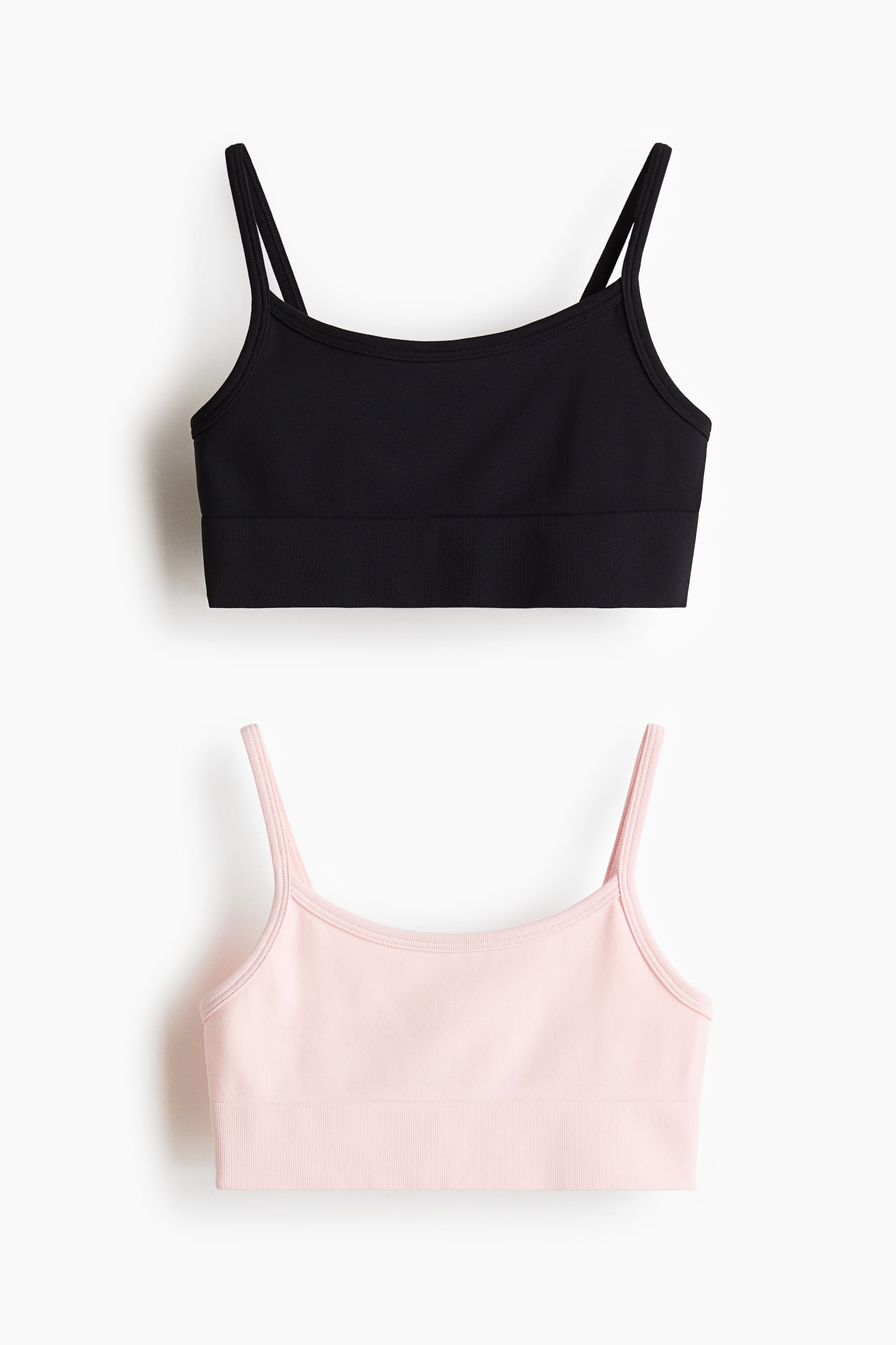 Grösseres Bild ansehen: Ein 2er-Pack Seamless Sports-Tops wird präsentiert, bestehend aus einem schwarzen Top und einem hellrosa Top. Beide frontal gezeigten Tops verfügen über dünne Spaghettiträger und ein breites, geripptes Bündchen am unteren Saum.