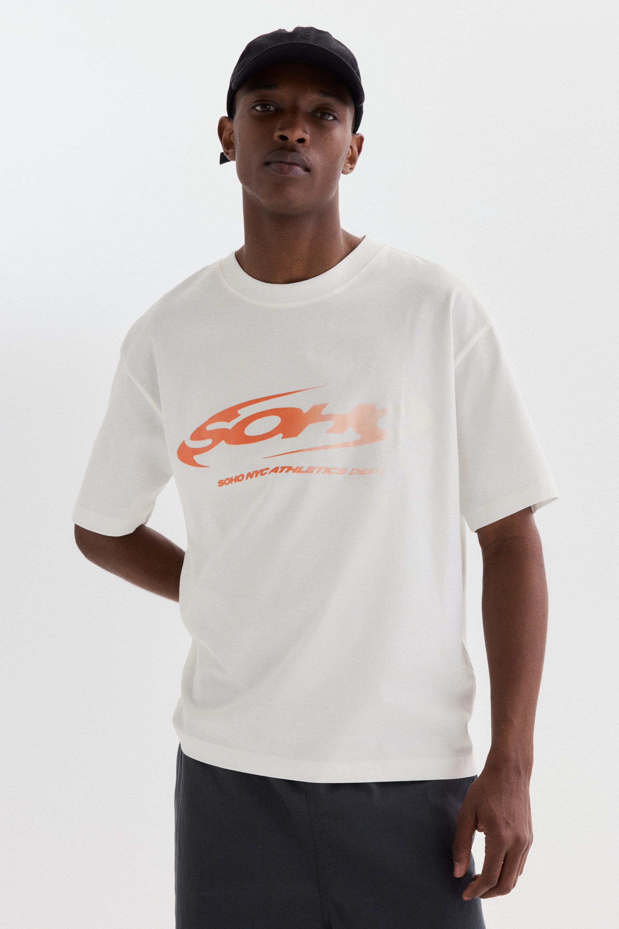 View larger image: A white short-sleeved t-shirt featuring a large, stylized orange gradient graphic with the text 'SOHO NYC ATHLETICS DEPT' on the front. The t-shirt is cut for a relaxed fit and has a crew neck.