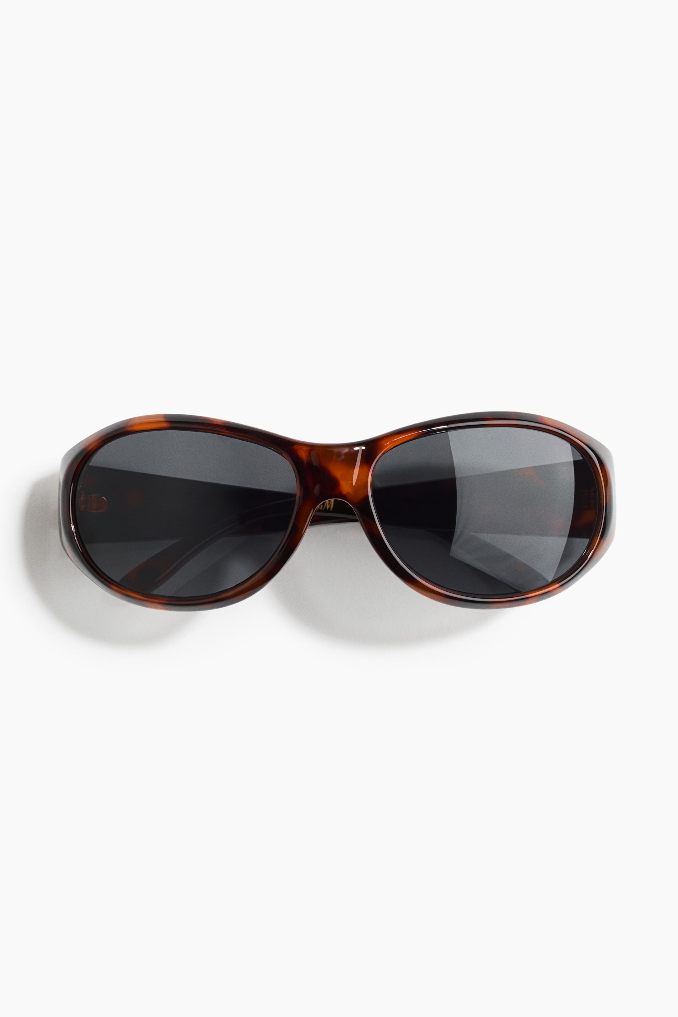 Agrandir l'image: Lunettes de soleil avec une monture écaille de tortue et des verres teintés foncés. La monture frontale présente une forme arrondie, légèrement incurvée.