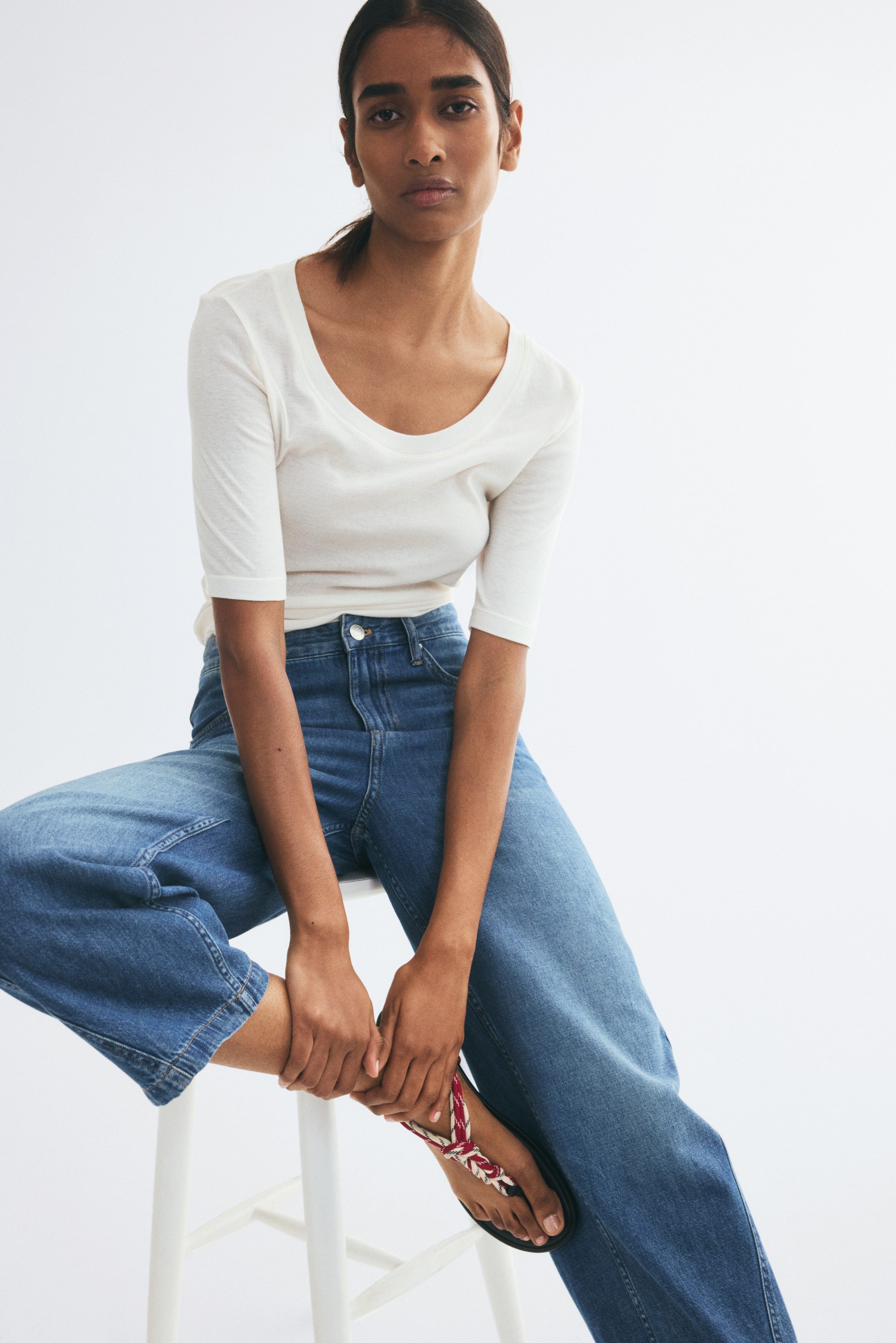 These blue denim jeans are shown from the front, featuring a regular waist with a button closure, a zip fly, and classic front scoop pockets. They feature curved, voluminous legs that taper toward the hems, with distinct side seams curving forward to define the relaxed fit.
