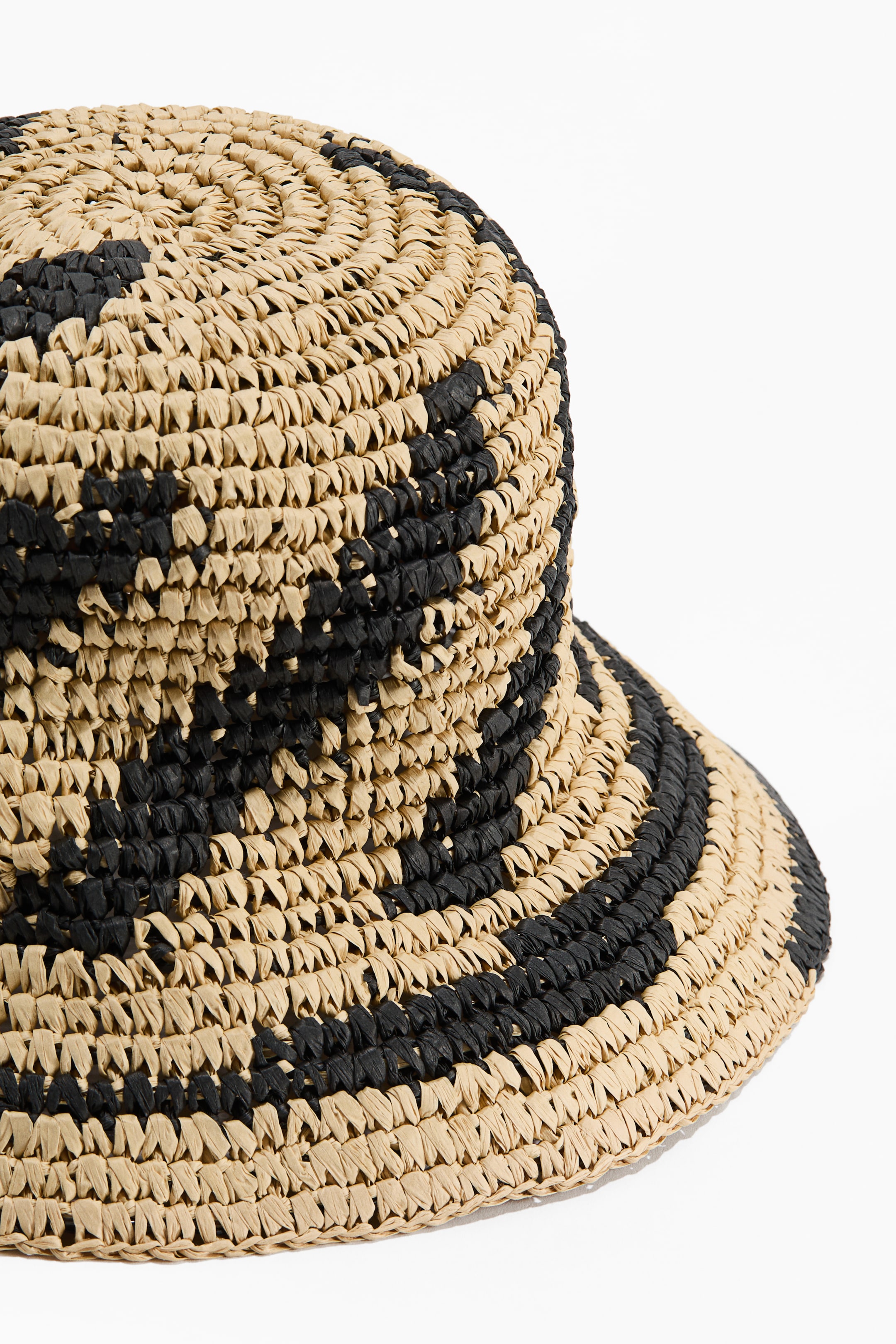 View larger image: A woven raffia bucket hat featuring a tan and black geometric pattern. It showcases a rounded crown and a downward-sloping brim.