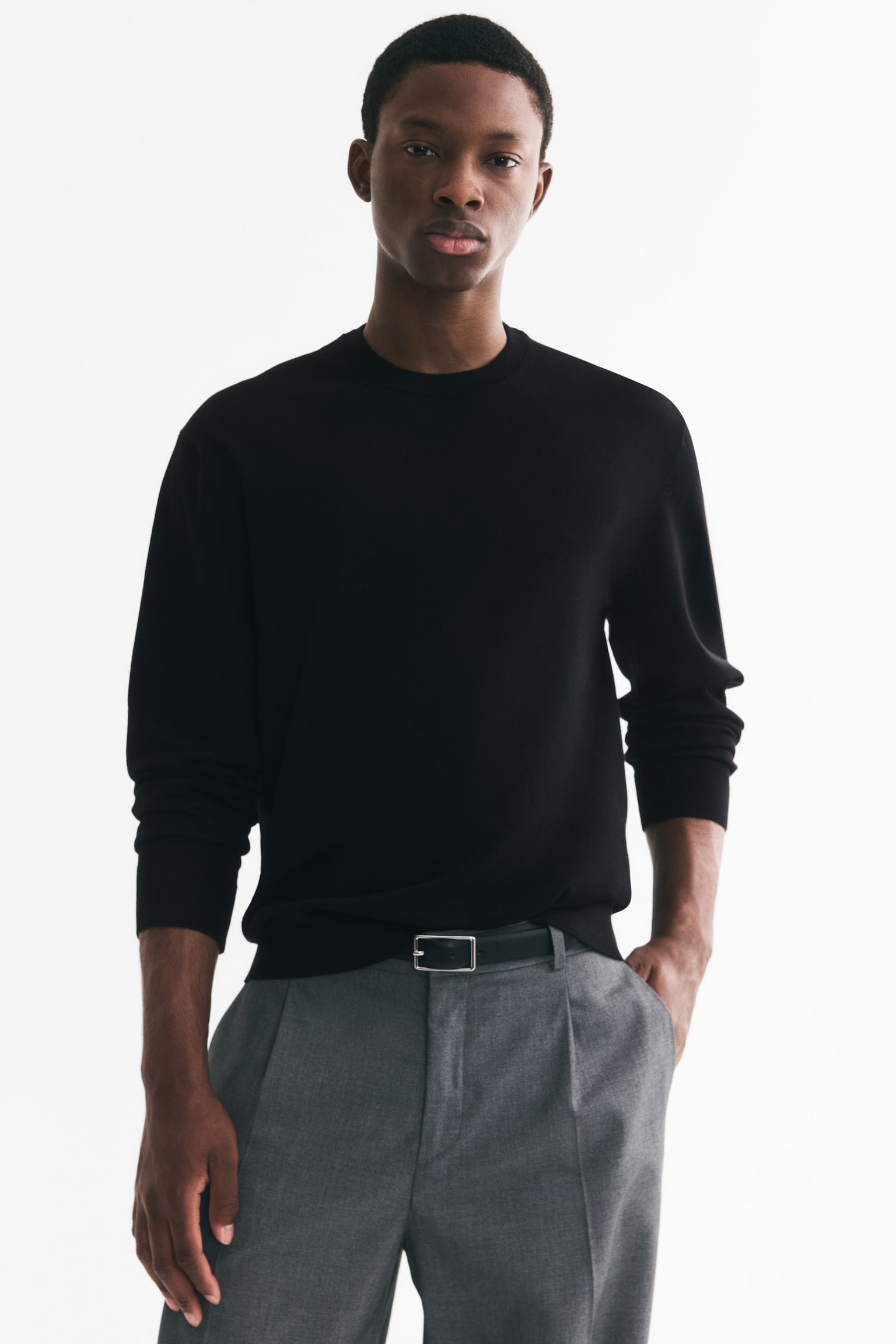 A black, fine-knit jumper is facing forward, featuring a crew neck, long sleeves with ribbed cuffs, and a ribbed hem. A small black H&M Regular Fit label is visible at the back of the neck. - 1