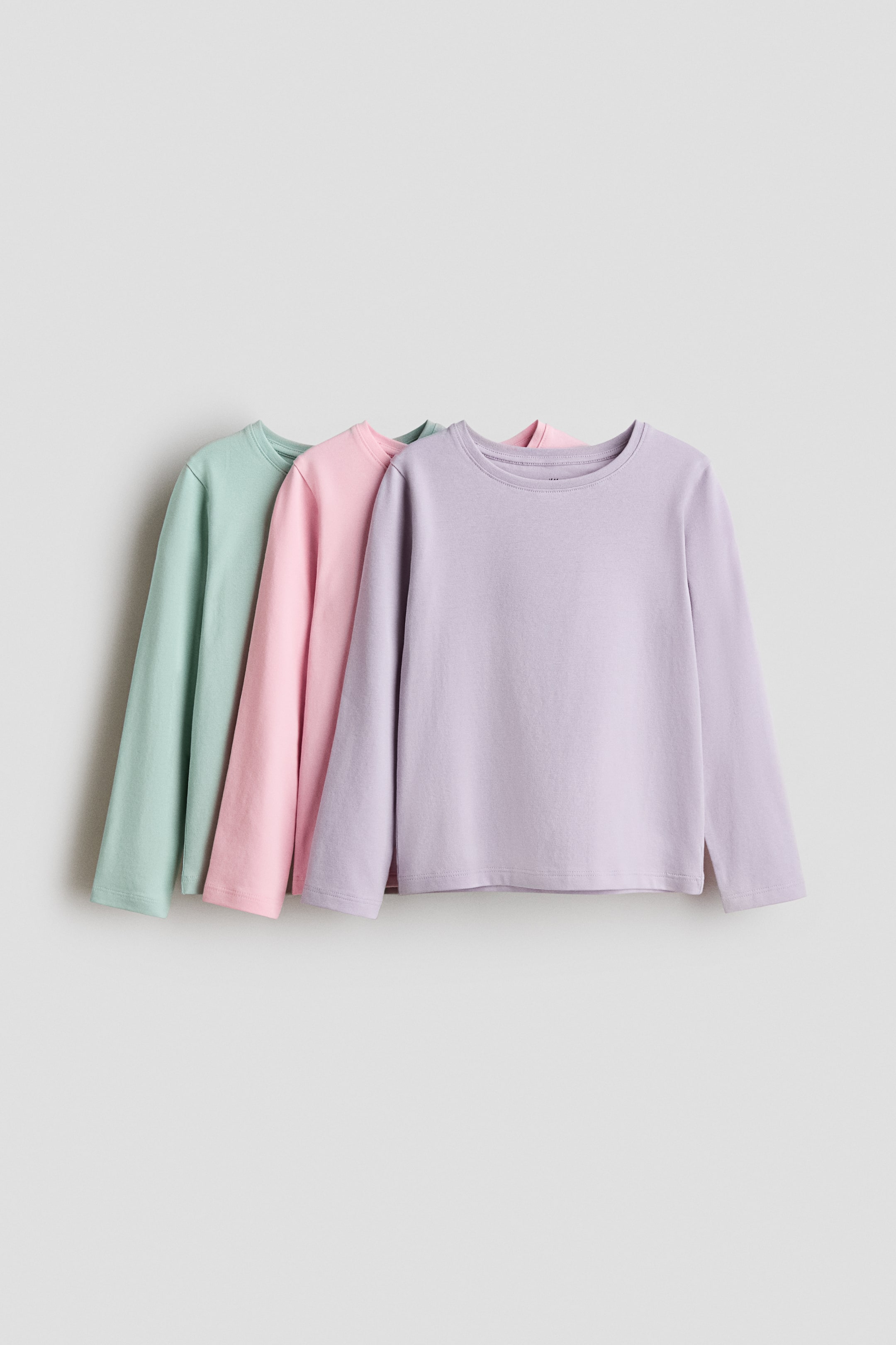 View larger image: Long-sleeved tops in soft cotton jersey are displaying their fronts, layered in mint green, pink, and lavender. Each top is featuring a crew neckline and long sleeves, with the front lavender top also presenting small side slits at its hem.