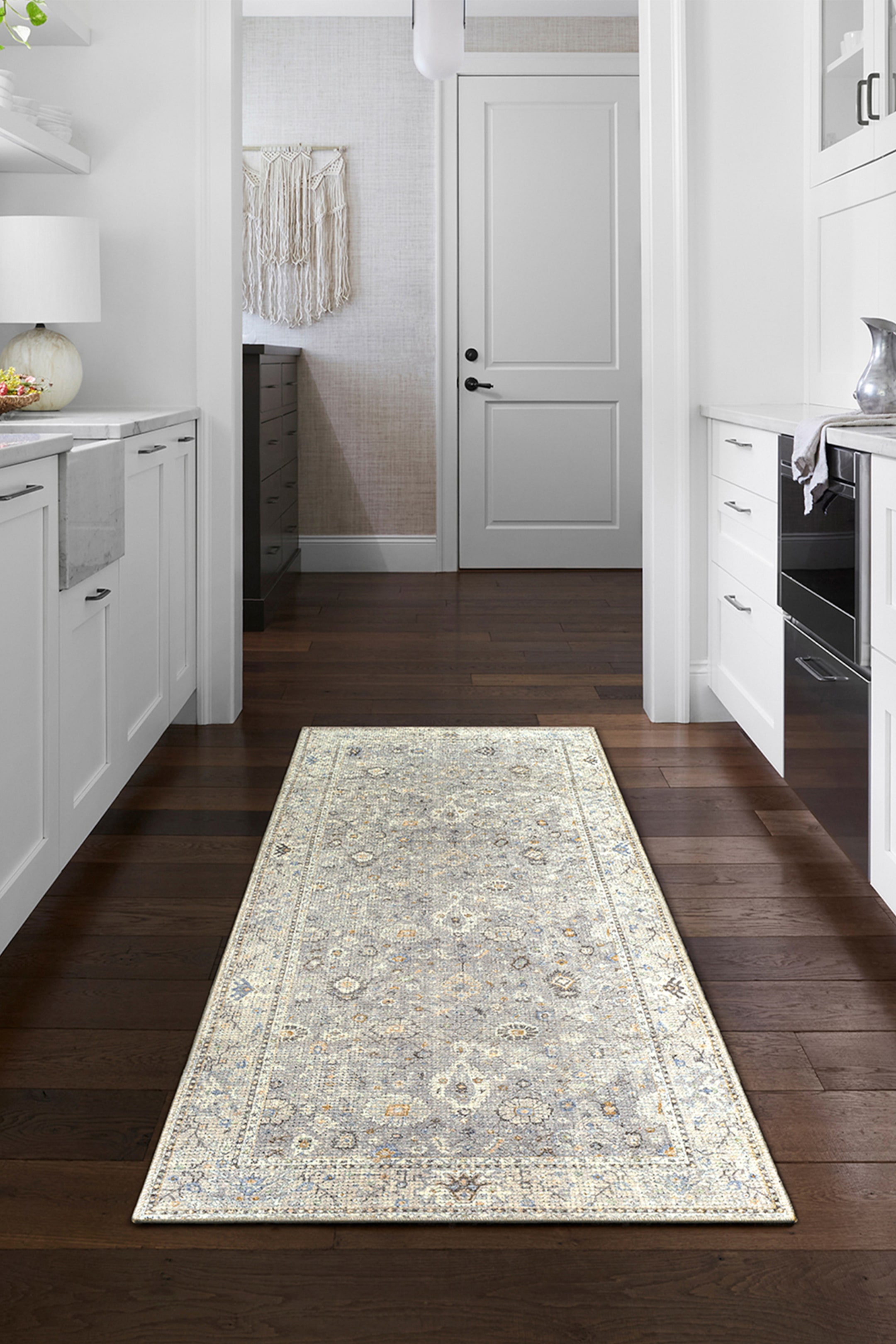 View larger image: A rectangular runner rug is laid flat on a dark hardwood floor, showcasing a distressed traditional pattern with a distinct border and central floral motifs in shades of light grey, cream, muted blue, and subtle orange accents.