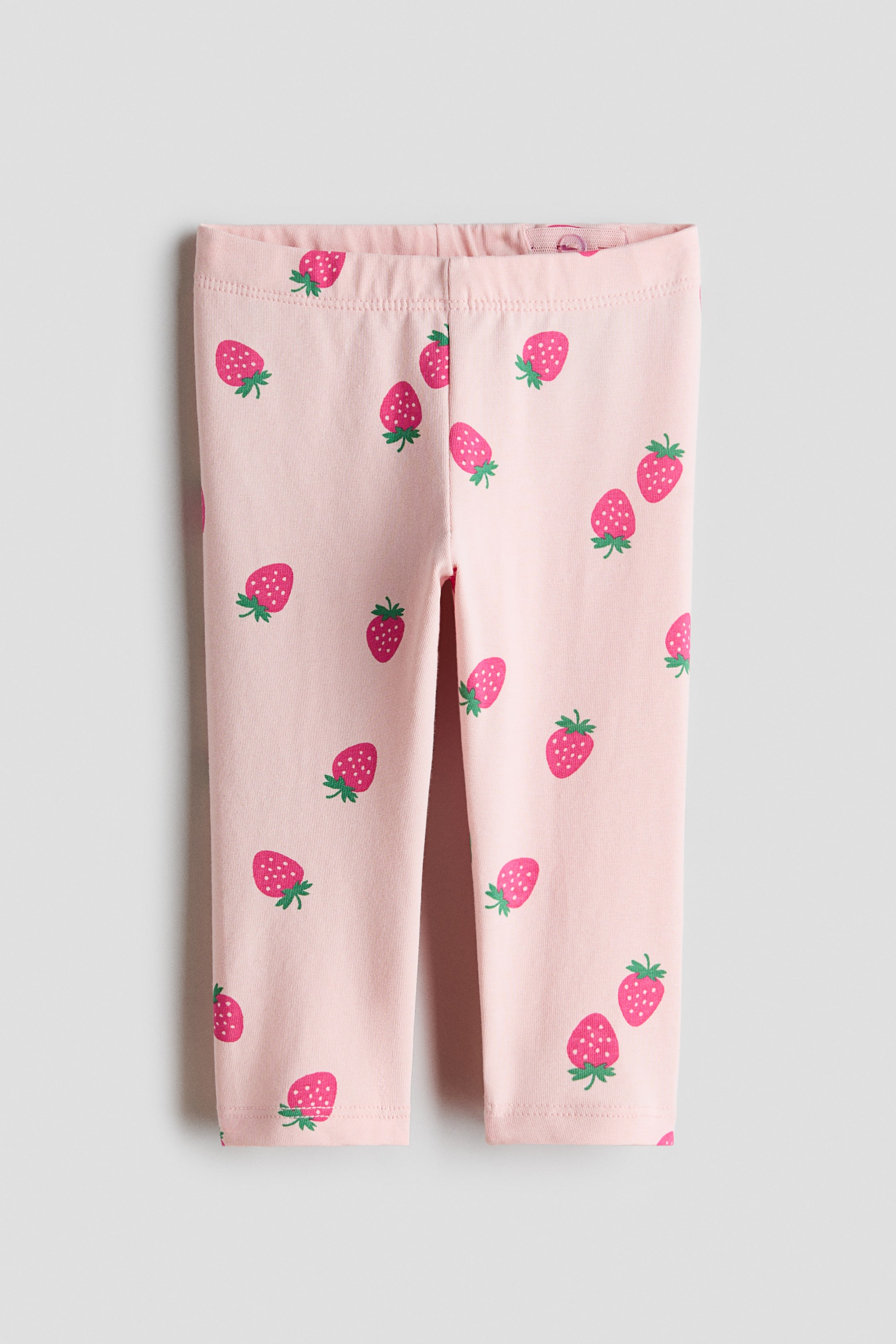 Xem ảnh lớn hơn: Leggings màu hồng có họa tiết in phủ toàn bộ hình những quả dâu tây đỏ với cuống xanh. Sản phẩm có chun eo co giãn và gấu quần may đơn giản ở cổ chân.