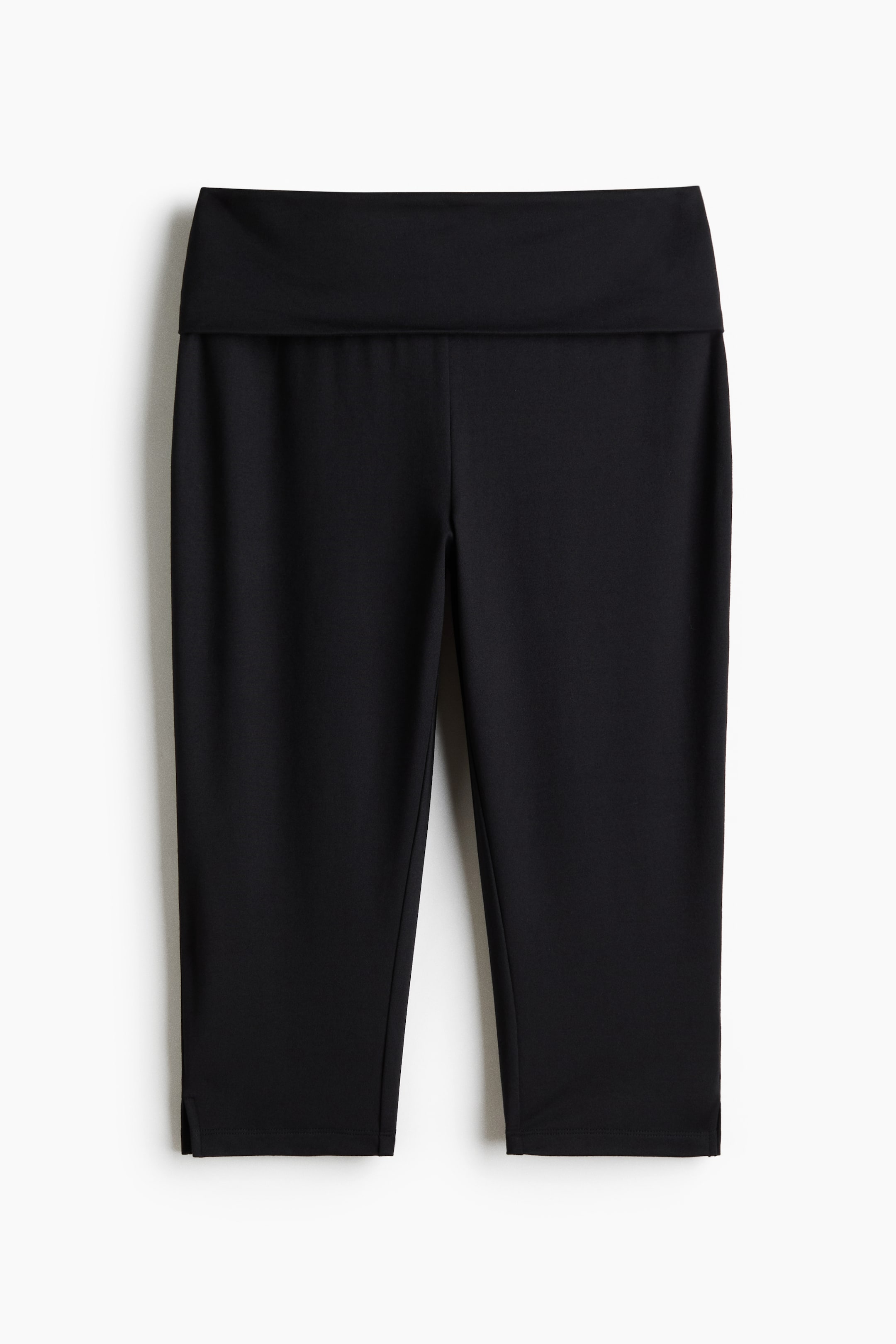 View larger image: Black capri leggings feature a wide, folded-over waistband and small side slits at the cuffs, viewed from the front.