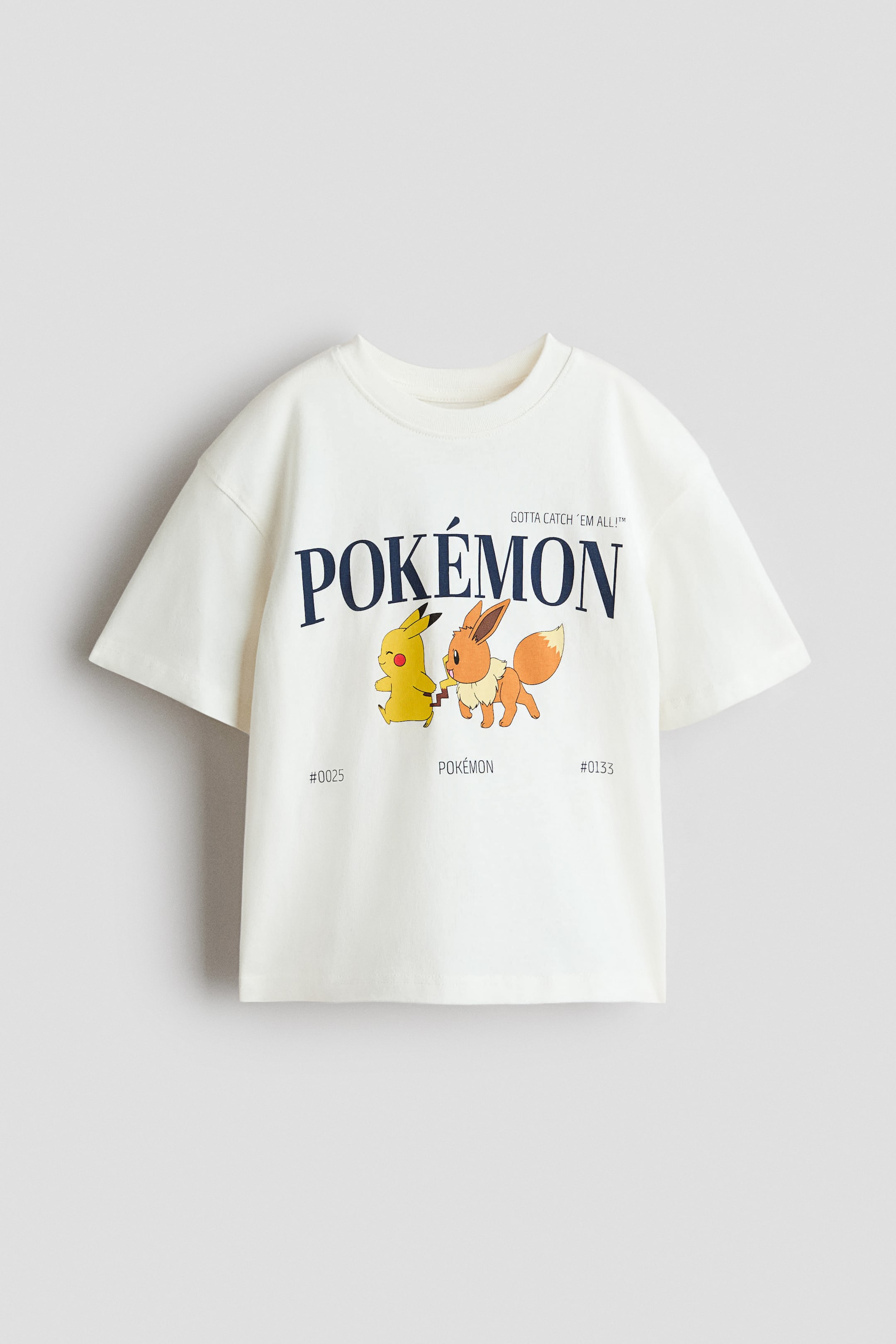 View larger image: An oversized t-shirt in soft, printed cotton jersey is shown from the front, featuring a ribbed trim around the neckline and dropped shoulders. The t-shirt is displaying a graphic print with the dark blue "POKÉMON" logo, a yellow Pikachu, and an orange-brown Eevee, along with the text "GOTTA CATCH 'EM ALL!?" and the numbers "#0025" and "#0133".