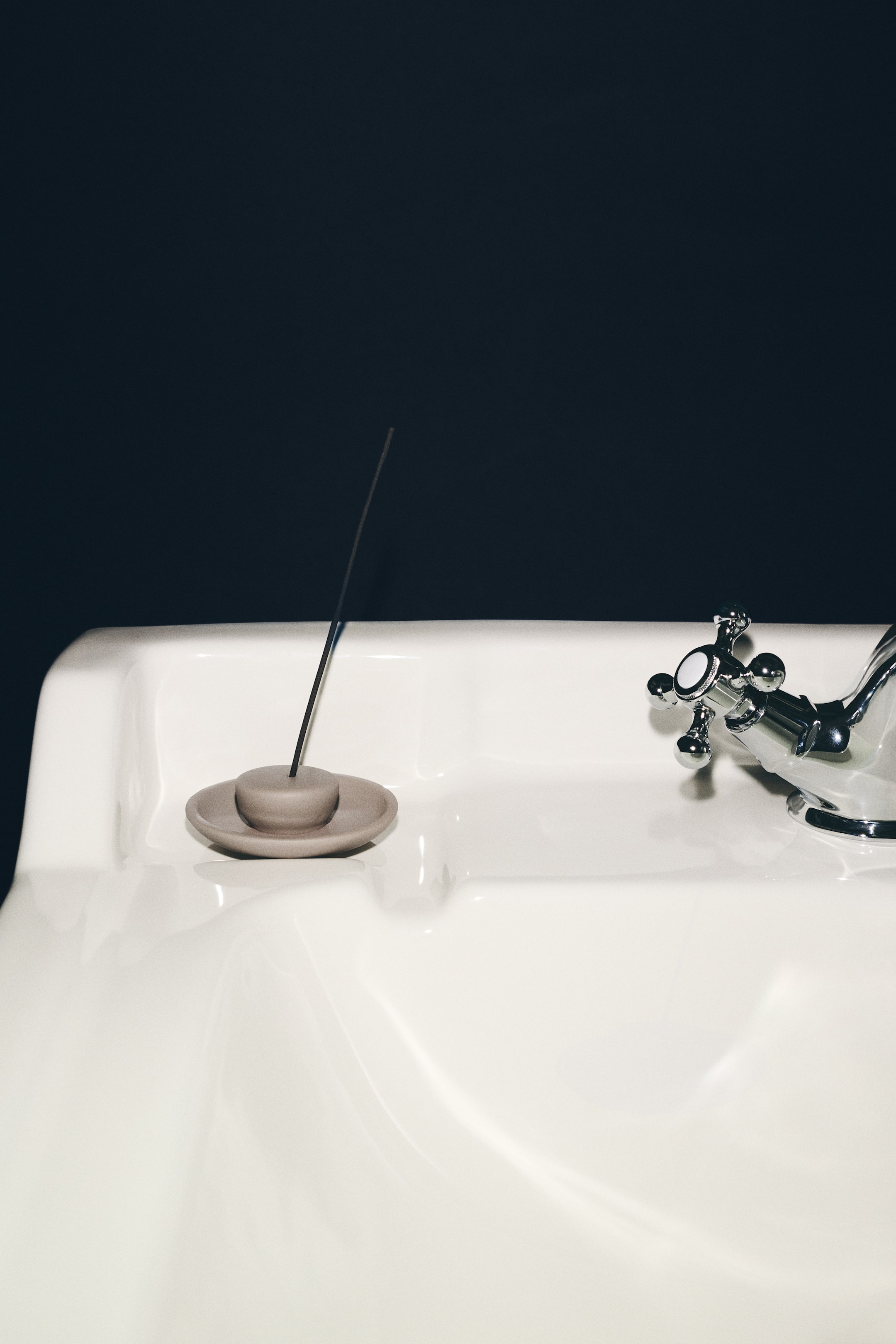 Agrandir l'image: Un porte-encens en grès beige, composé d’une base peu profonde en forme de soucoupe et d’un petit dôme central arrondi, repose sur une surface en céramique blanche tout en maintenant un bâton d’encens foncé à la verticale.