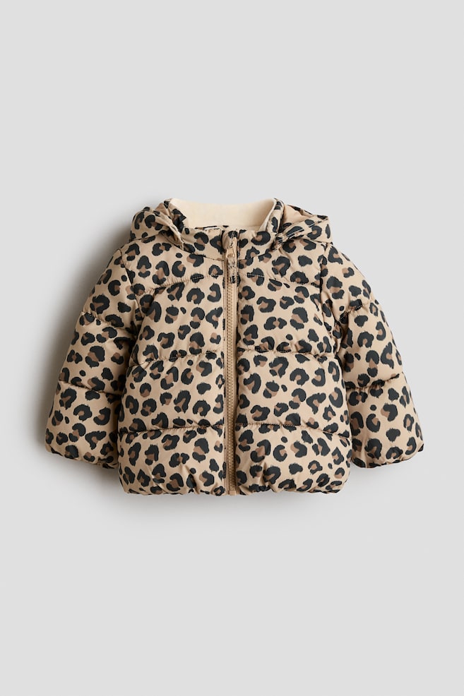 Eine Steppjacke wird in der Vorderansicht gezeigt und verfügt über ein allover Leopardendruckmuster in Hellbraun, Dunkelbraun und Schwarz. Sie ist mit einem durchgehenden Reißverschluss bis zum Stehkragen, einer gefütterten Kapuze sowie elastischen Ärmelbündchen und einem elastischen Saum ausgestattet. - 1