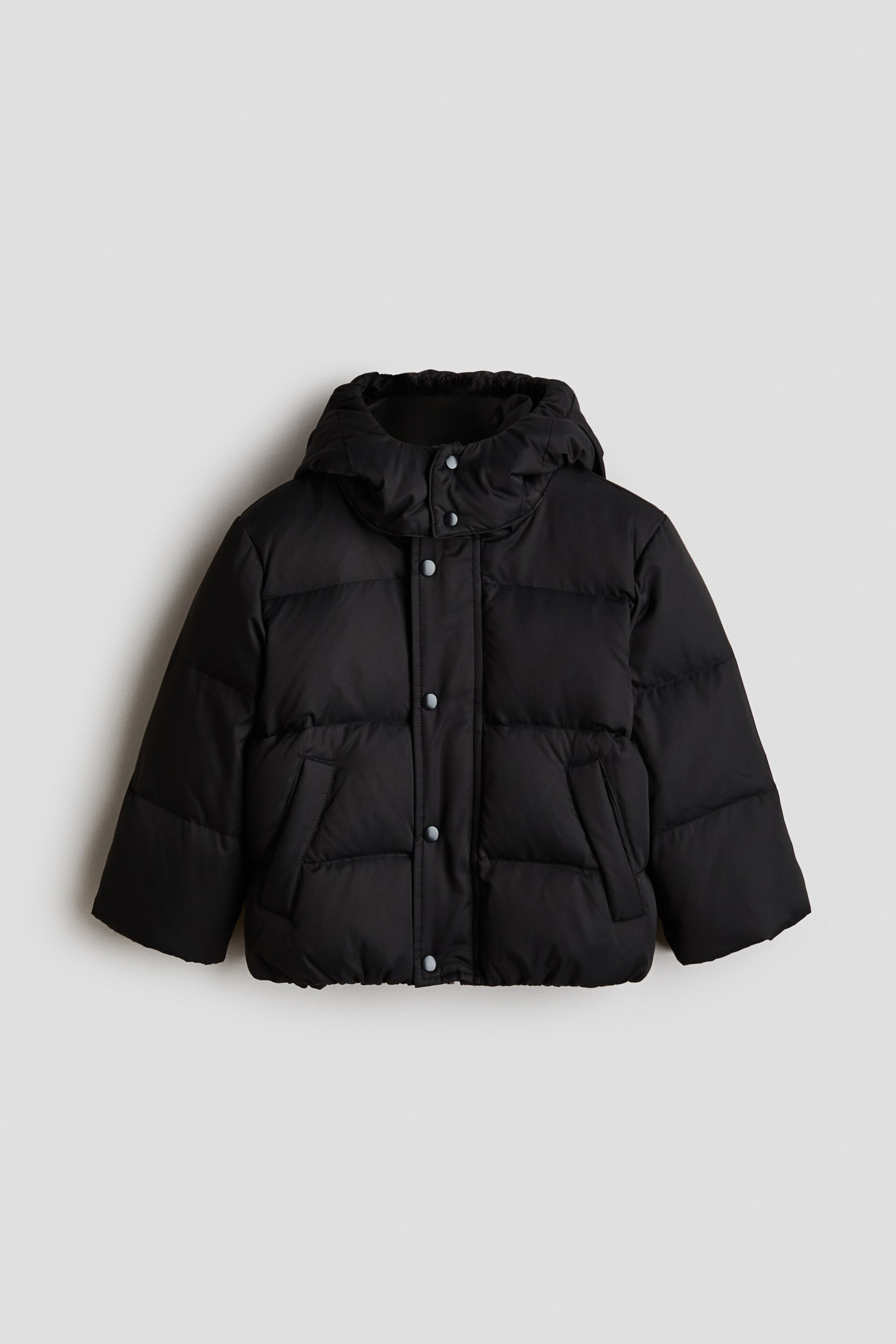 Größeres Bild anzeigen: Eine schwarze Steppjacke ist von vorne zu sehen und verfügt über eine angesetzte Kapuze, ein gepolstertes Design mit horizontaler Steppung, einen Frontverschluss mit hellen Druckknöpfen und zwei schräg angesetzte Fronttaschen.