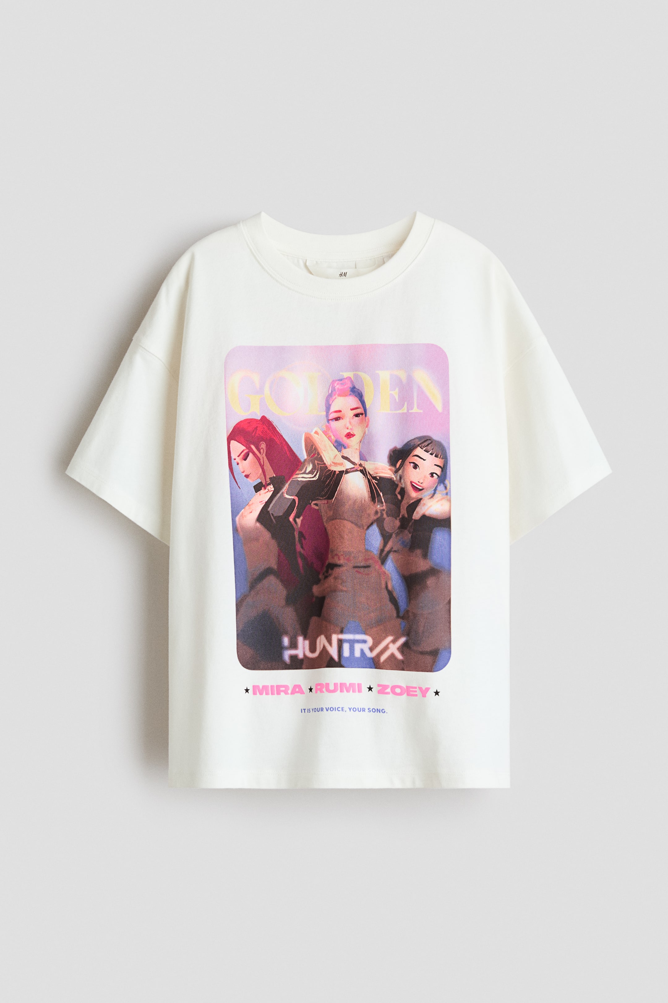 Größeres Bild ansehen: Ein übergroßes T-Shirt wird von vorne präsentiert, gefertigt aus einem leichten cremefarbenen Baumwolljersey. Es verfügt über einen großen Grafikdruck auf der Vorderseite, der drei stilisierte weibliche Figuren zeigt, mit den Texten „GOLDEN“, „HUNTRAX“, „MIRA * RUMI * ZOEY“ und „IT IS YOUR VOICE, YOUR SONG“. Das T-Shirt ist mit einem runden, gerippten Halsausschnitt und überschnittenen Schultern designt, was ihm eine entspannte Passform verleiht.