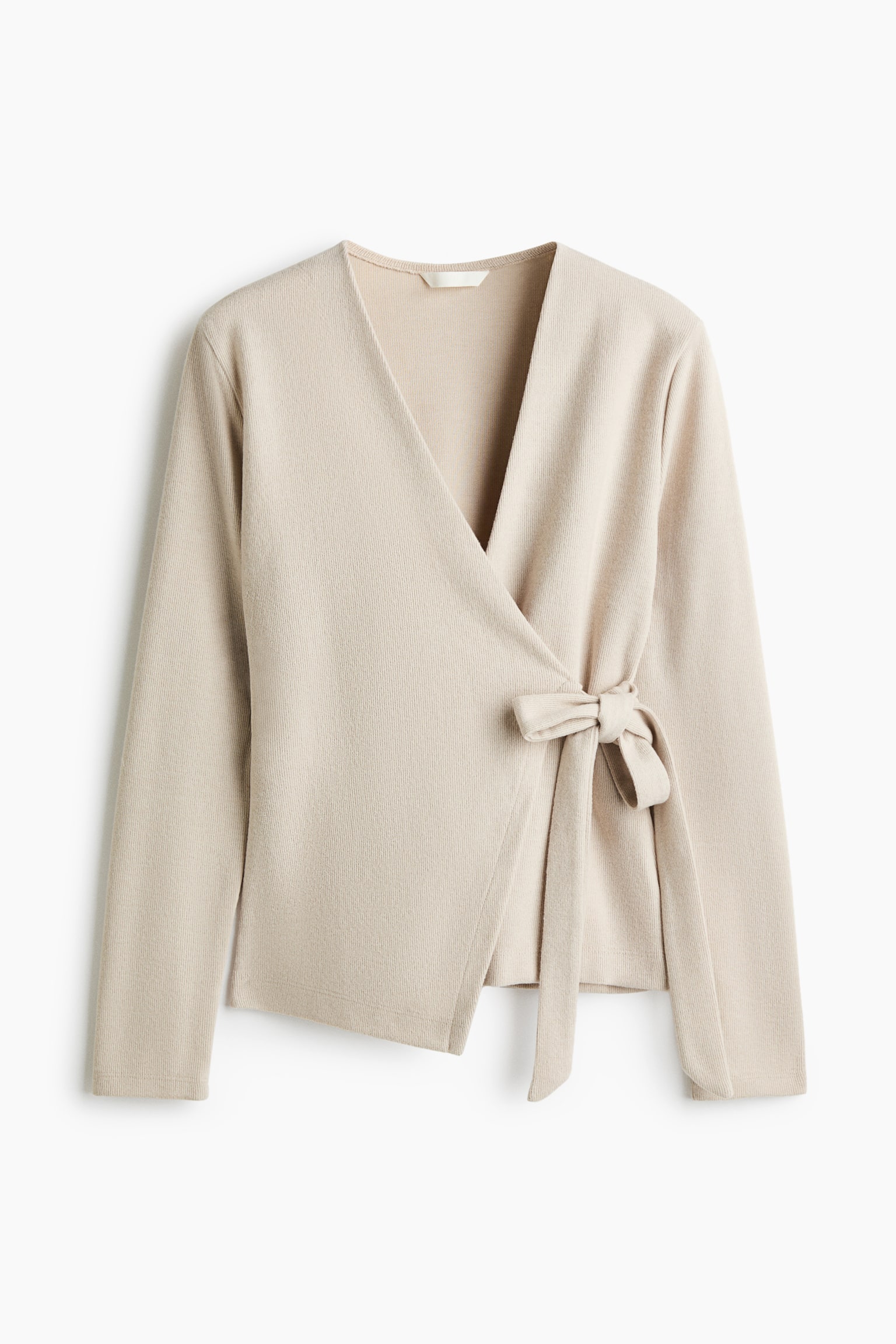 A light beige wrap cardigan in a soft knit is shown from the front, featuring a V-neckline and long sleeves. The cardigan is fastened on one side with a wide tie bow, showcasing its asymmetrical wrap-front design.