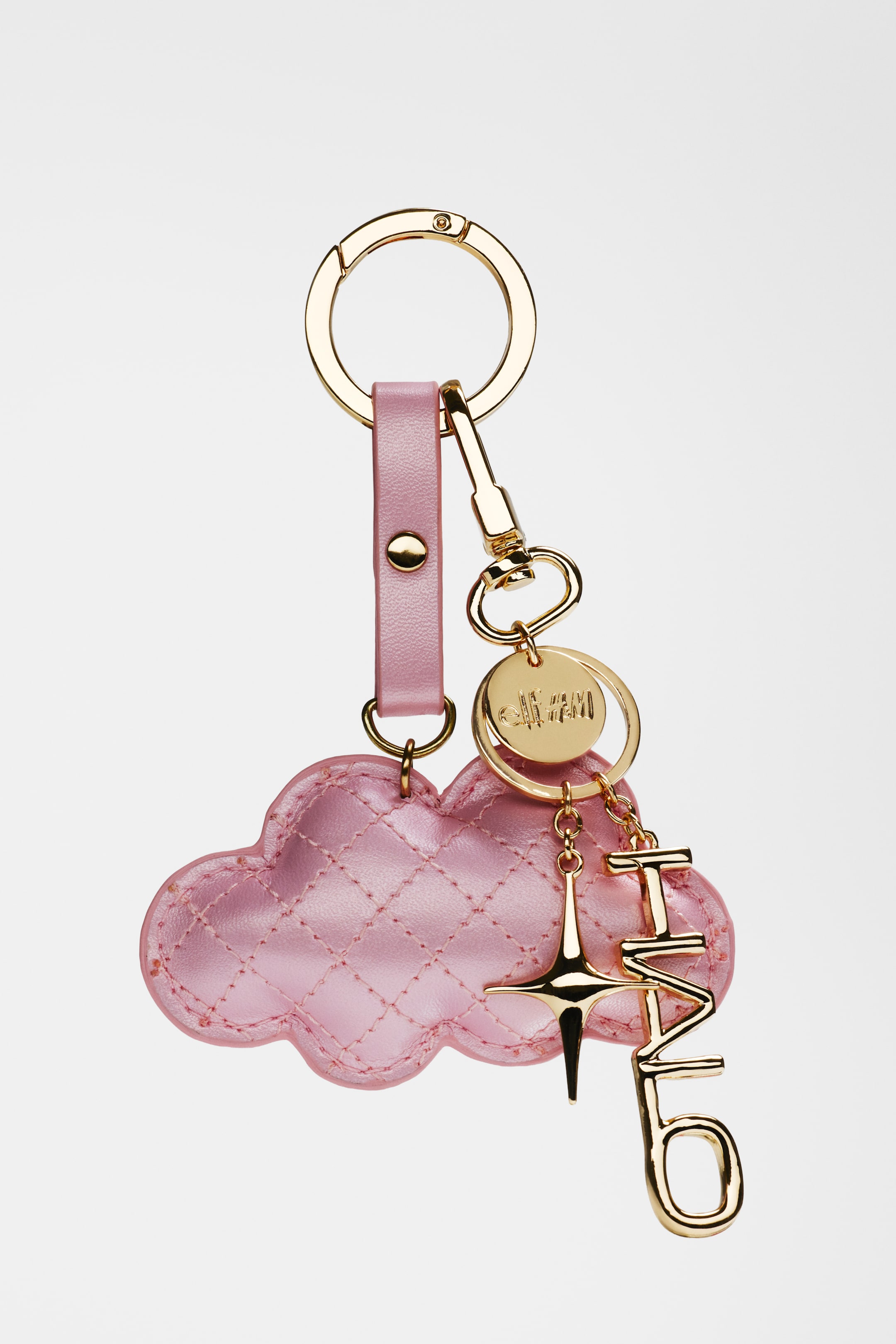 Größeres Bild ansehen: Ein Schlüsselanhänger hängt vertikal und verfügt über einen goldfarbenen Metallring, der an einem pinkfarbenen Lederband befestigt ist, das durch einen goldfarbenen Druckknopf gesichert wird. Ein goldfarbener Karabinerhaken hält mehrere Anhänger, darunter einen pinkfarbenen, wolkenförmigen Anhänger mit gesteppten Nähten, eine runde goldfarbene Scheibe mit einem eingravierten Design, einen goldfarbenen, sternförmigen Anhänger und goldfarbene Buchstabenanhänger, die 'IT'S MLO' buchstabieren.