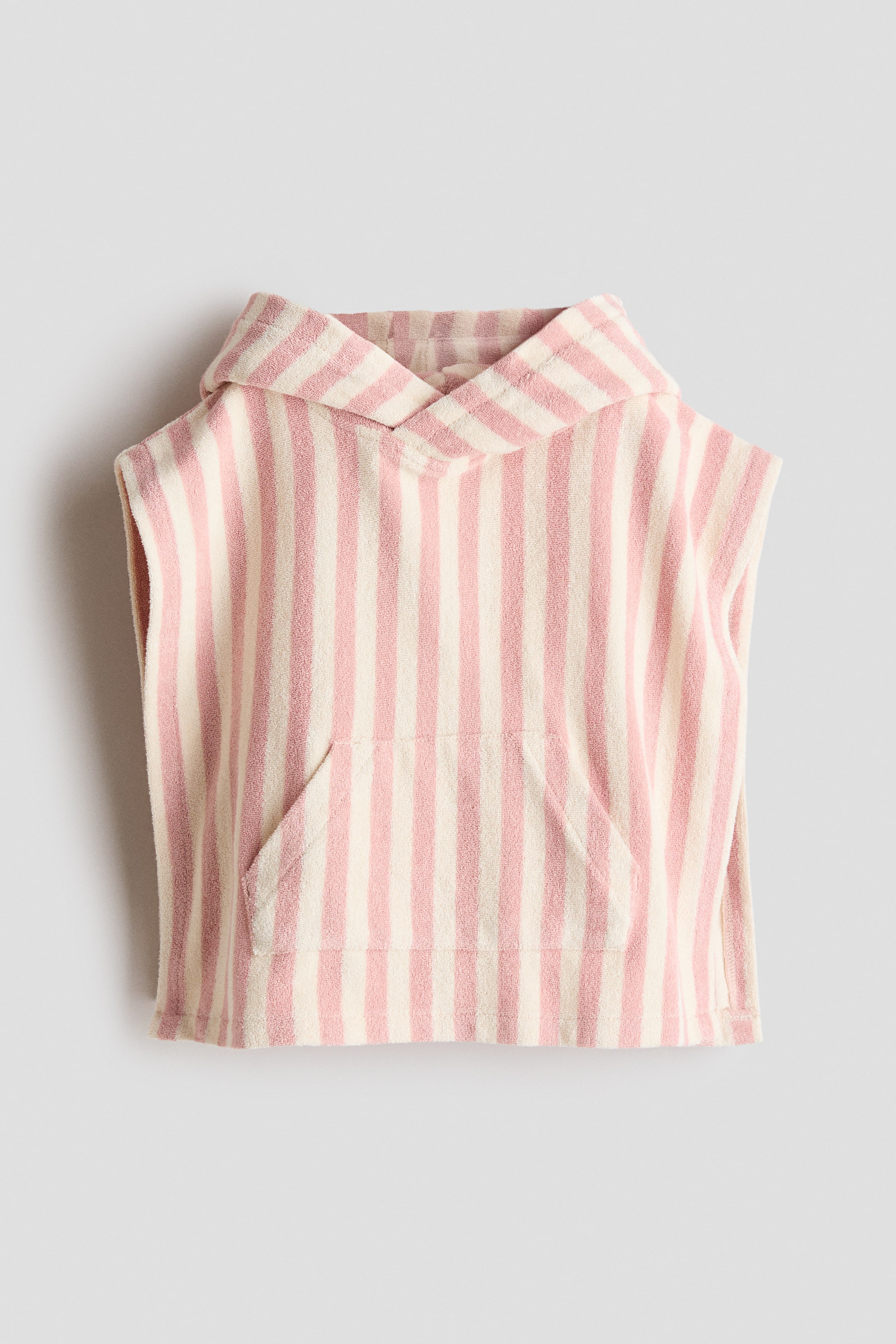 Größeres Bild anzeigen: Ein Kapuzenhandtuch-Cape wird von vorne gezeigt, mit vertikalen Streifen in Rosa und Creme und einer sichtbaren Frottee-Textur. Es verfügt über eine Kängurutasche auf der Vorderseite und eine angenähte Kapuze, mit offenen Seiten.