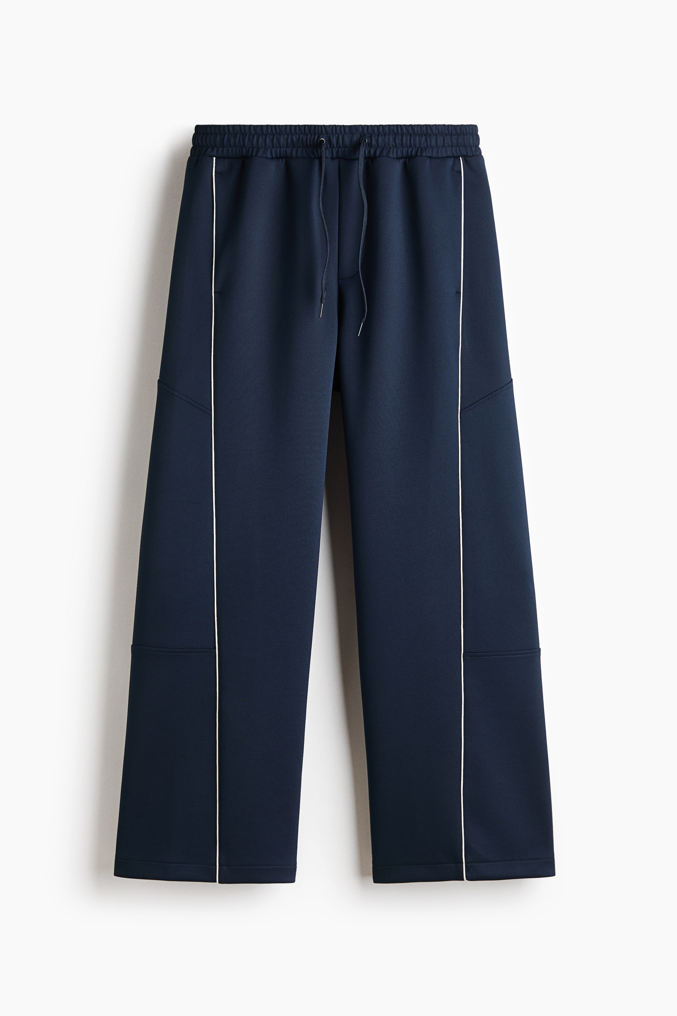 View larger image: Navy blue wide-leg trousers are shown from the front, featuring an elastic waistband with matching drawstrings and a relaxed, straight-leg fit. The design is detailed with contrasting white vertical piping running down the center of each leg and subtle horizontal paneling on the sides.