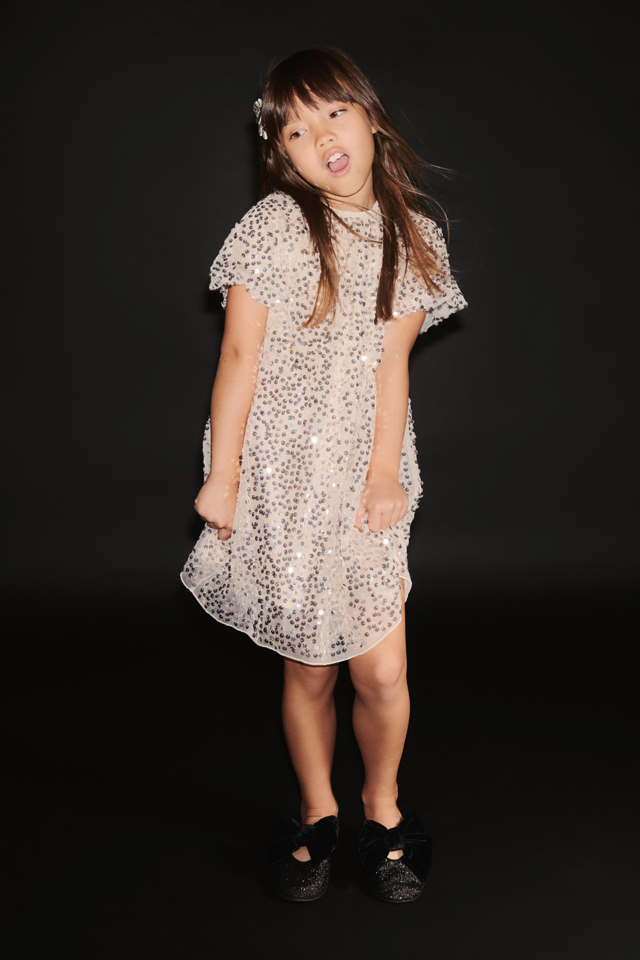 View larger image: An A-line dress in light pink sequin-covered mesh is shown from a front-facing angle, featuring a round gathered neckline and short balloon sleeves with elasticated cuffs.
