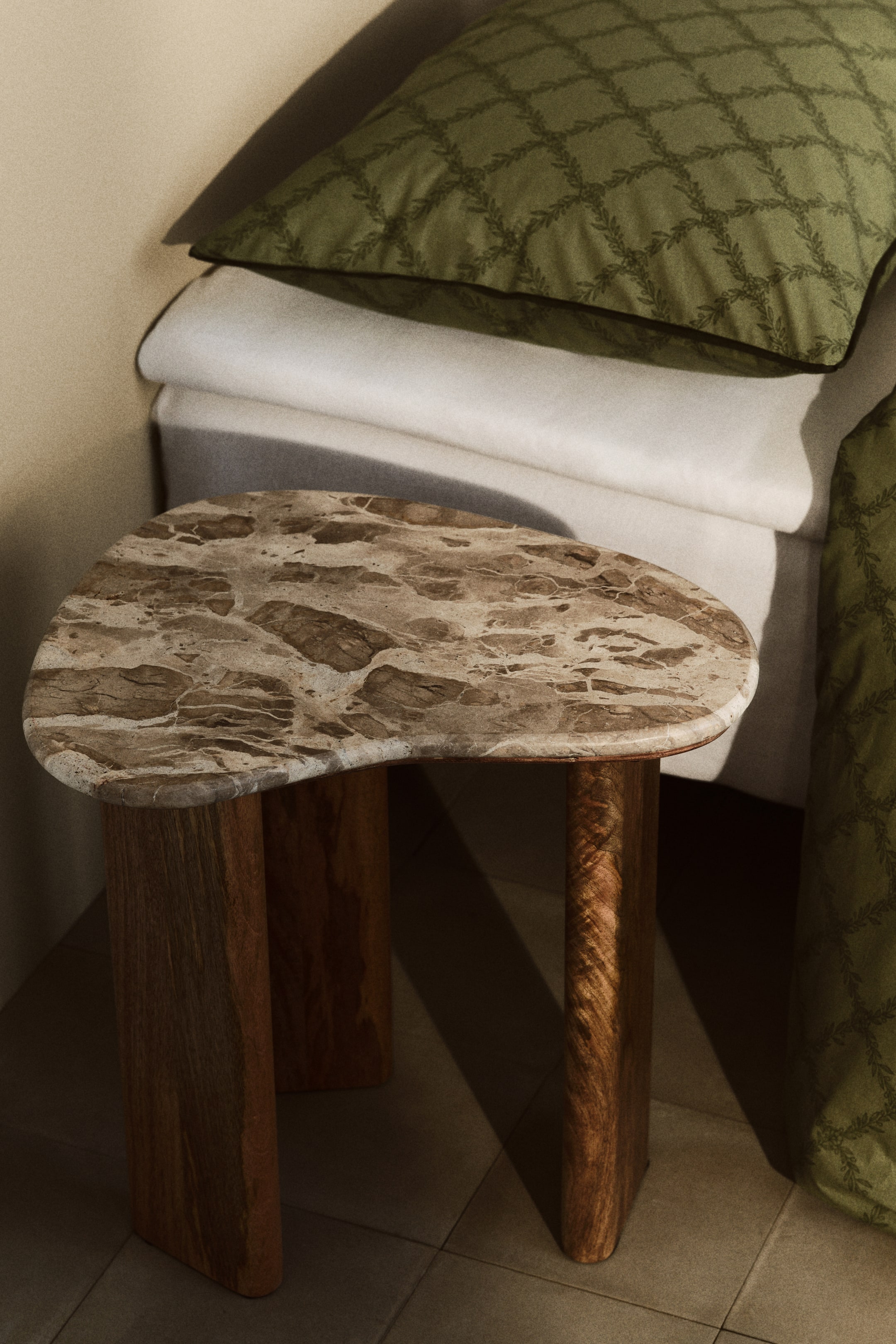 Zobacz większy obraz: Stolik boczny jest lekko skierowany do przodu, prezentując nieregularny, organicznie ukształtowany marmurowy blat z brązowymi i beżowymi żyłkami. Dwie grube, prostokątne drewniane nogi z widocznym usłojeniem podtrzymują blat.