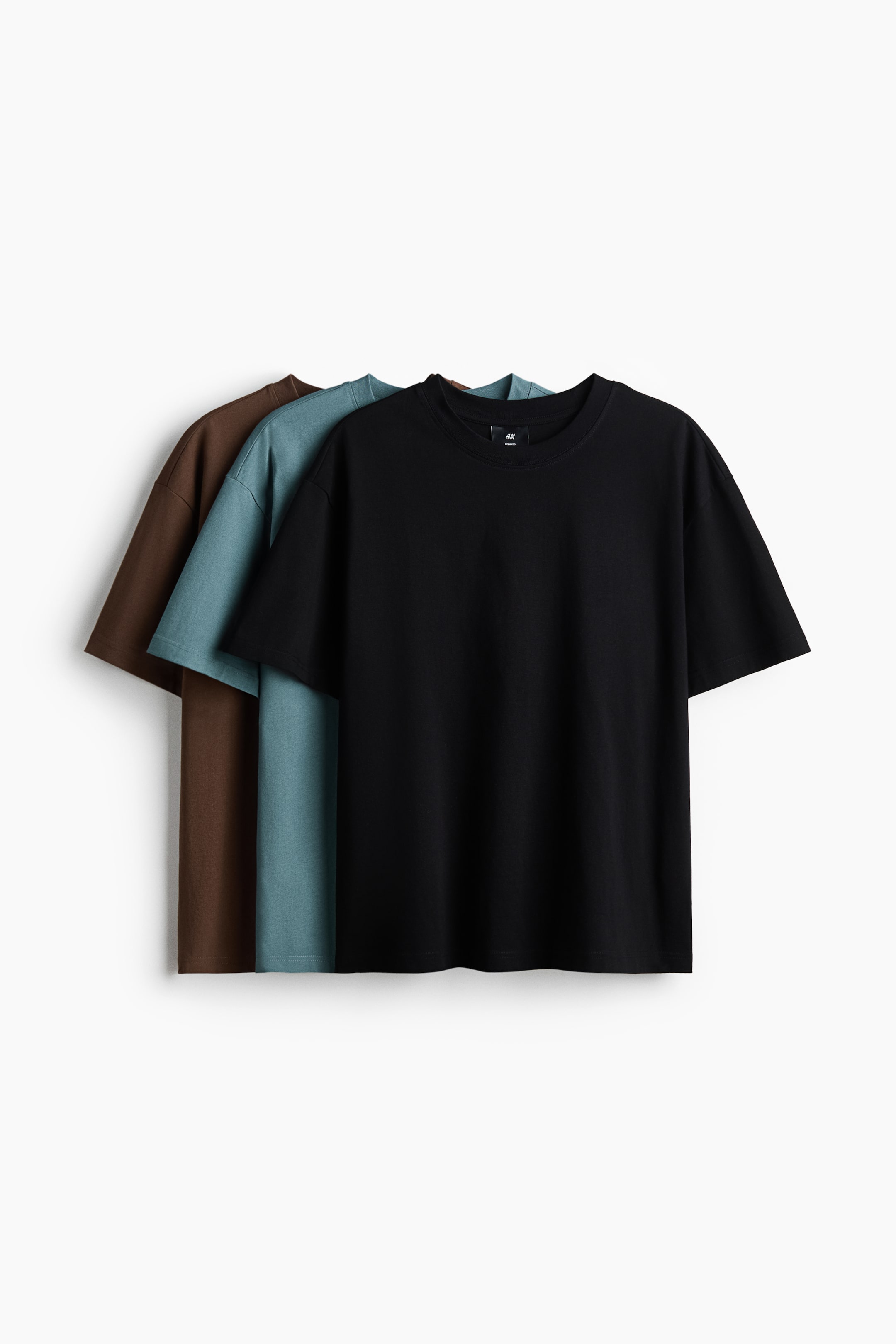 Agrandir l'image: Trois t-shirts à manches courtes et col rond sont présentés superposés, tous orientés vers l'avant. Le t-shirt de devant est noir, présentant une coupe décontractée, avec un t-shirt bleu sarcelle visible derrière lui et un t-shirt marron derrière celui-ci.