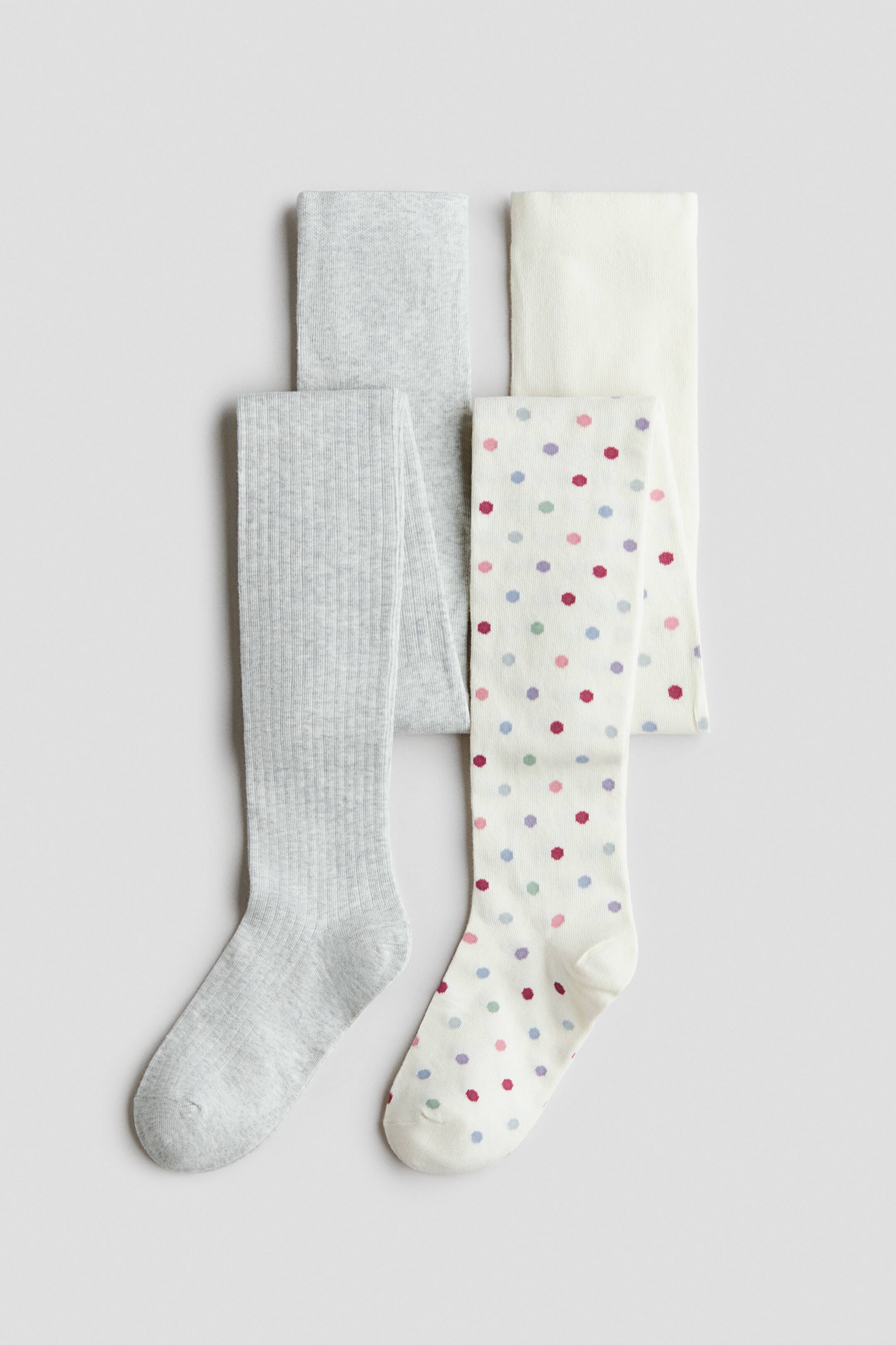 Agrandir l'image: Quatre paires de collants en maille sont disposées à plat, mettant en avant une paire côtelée gris clair et une paire blanc cassé ornée de pois multicolores à l’avant. Une paire gris clair unie et une paire blanc cassé unie sont soigneusement pliées derrière elles.