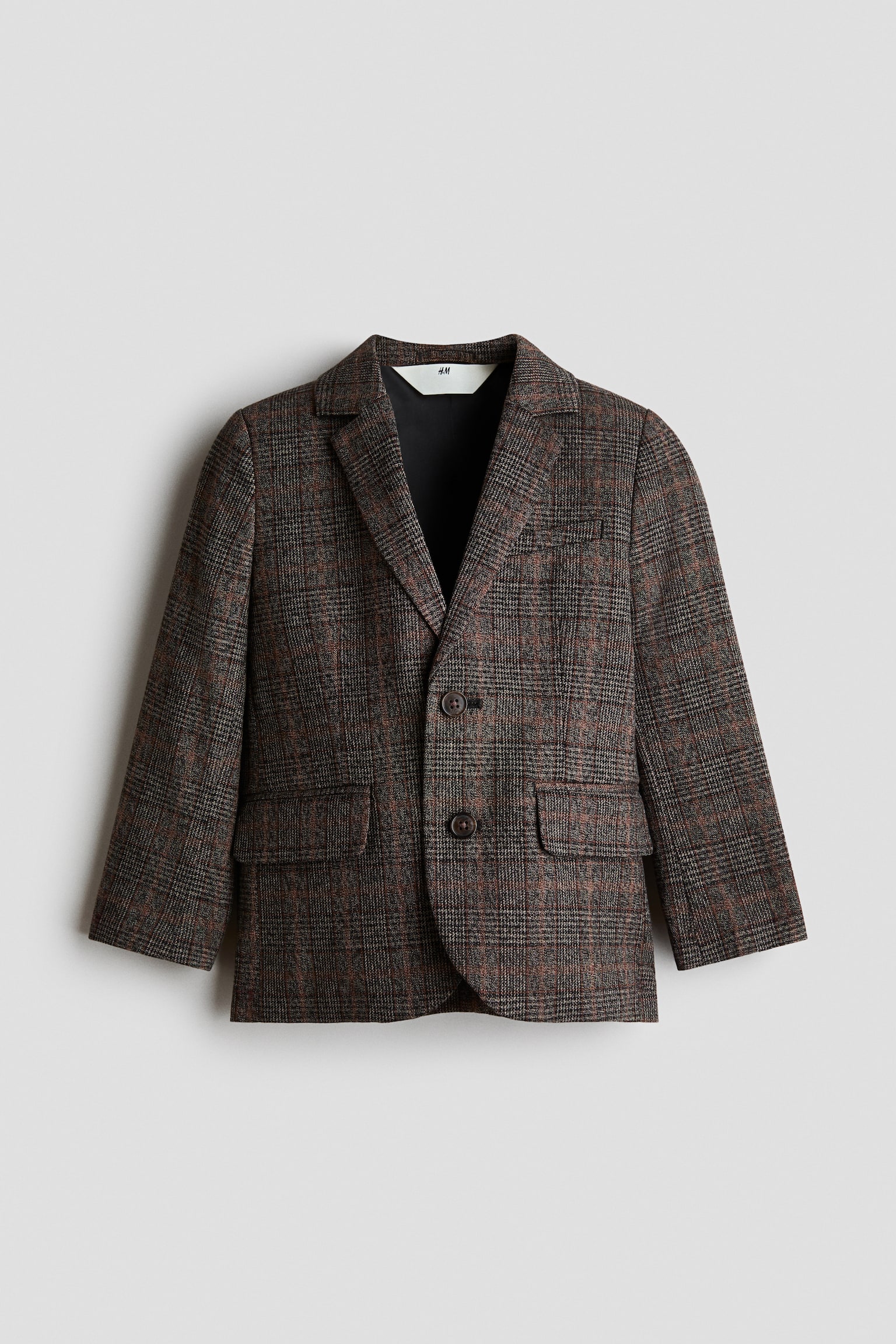 A woven cotton-linen blend jacket is shown from the front, featuring a brown and grey plaid pattern with notch lapels and a two-button front fastening. The design includes a mock chest pocket, two front mock flap pockets, and a dark interior lining visible at the collar.