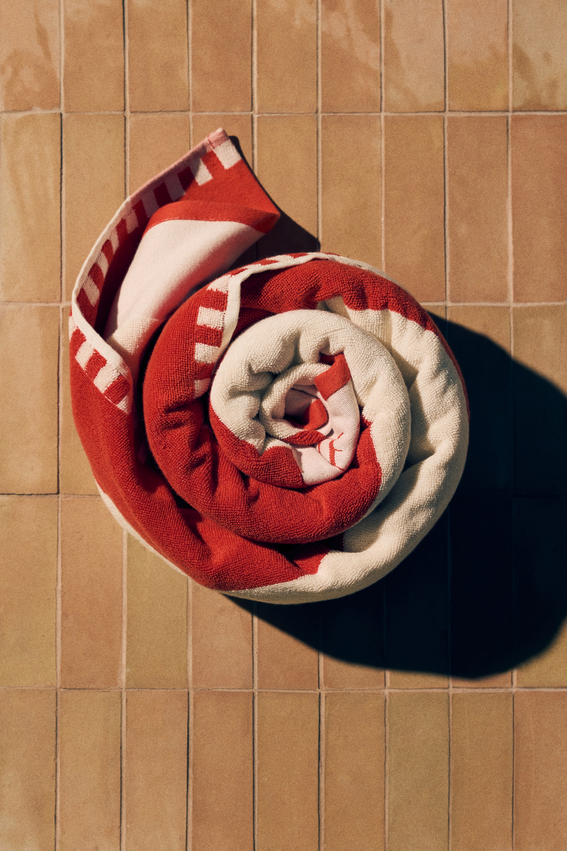Ver imagen más grande: Una toalla de playa se está enrollando en espiral. Presenta un patrón de rayas rojas y blancas y una textura suave de algodón rizo. Un motivo de texto rojo es visible en una sección blanca cerca del centro del rollo, y la toalla muestra bordes tejidos.