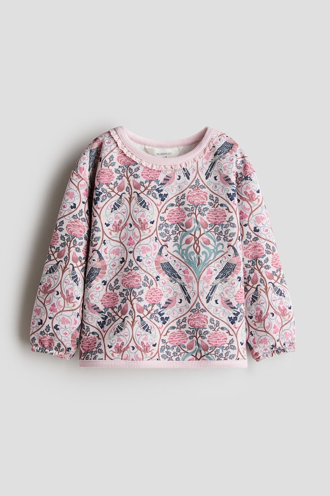 A pink long-sleeved sweater is shown from the front, featuring an intricate all-over print of birds and flowers in pink, blue and green hues. The sweater is designed with a round neckline adorned with a delicate scalloped trim, dropped shoulders, elasticated cuffs and a ribbed hem. - 1