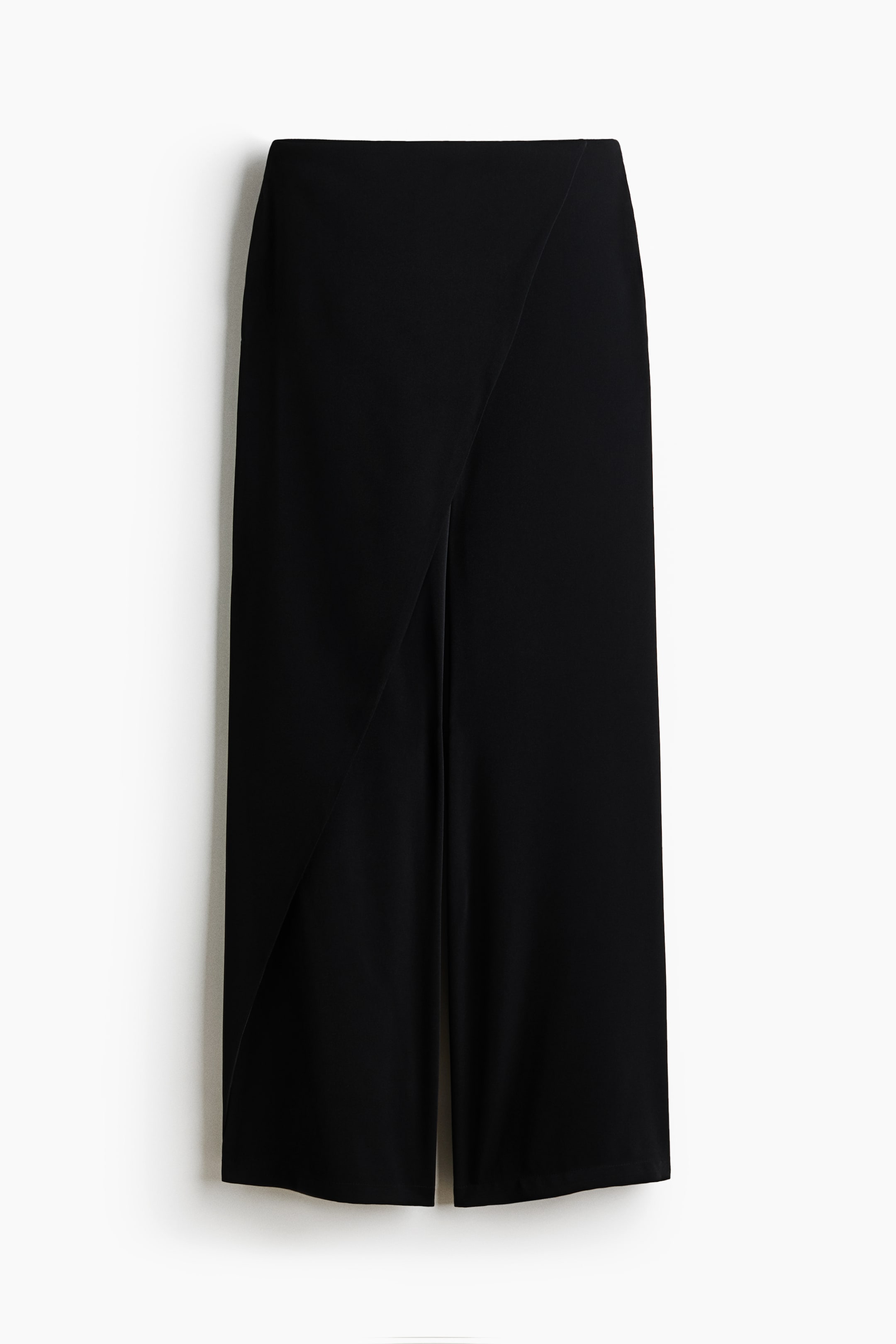 View larger image: Black wide-leg trousers are showcased from the front, featuring a smooth fabric and a cropped length, while an overlapping panel creates an asymmetrical front design with a diagonal line from the left hip downwards.