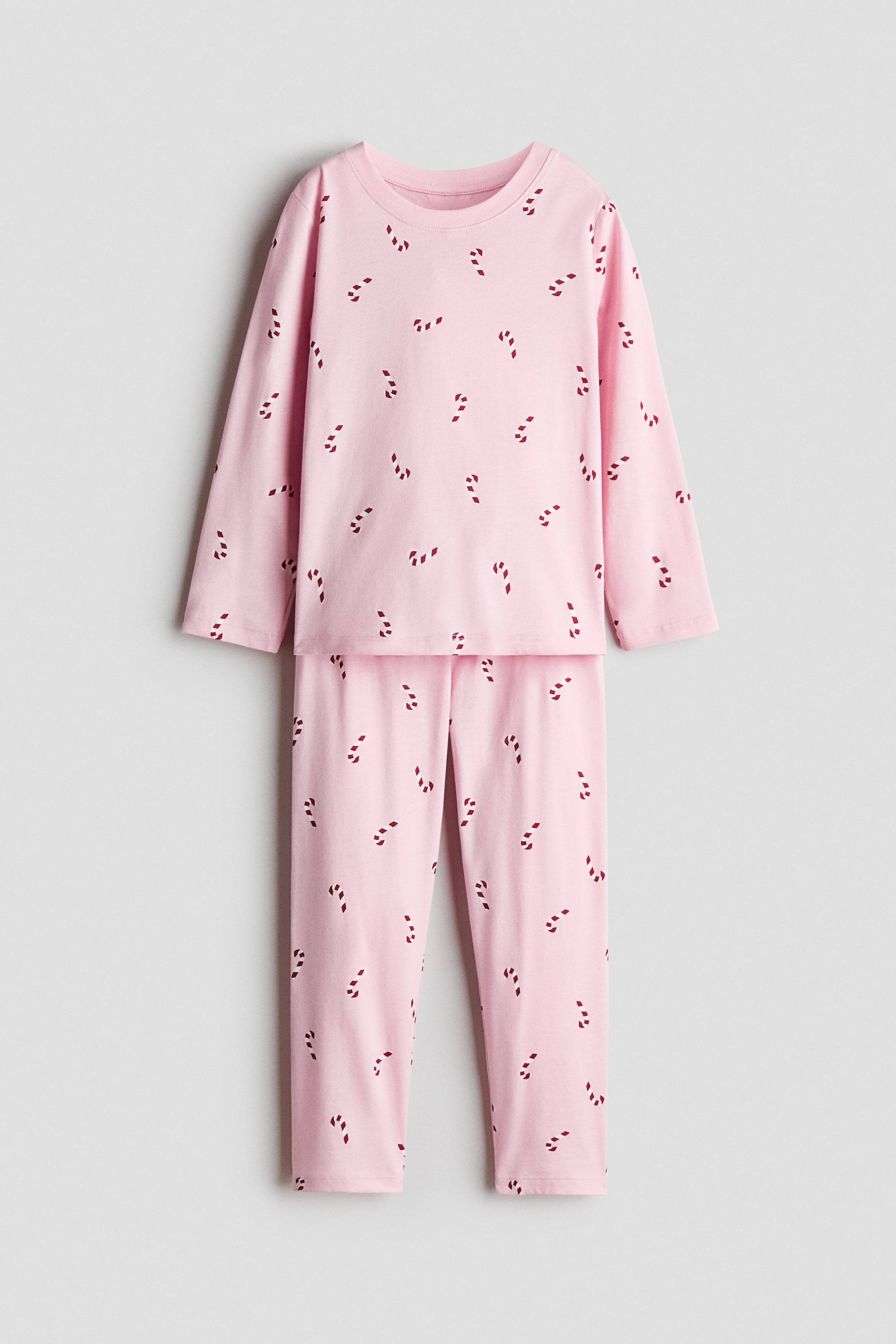 View larger image: A two-piece pyjama set in light pink cotton jersey is shown from the front, featuring an all-over print of tiny red-and-white striped candy canes. The set consists of a long-sleeved top with a round, narrow-trimmed neckline and matching long trousers with straight hems.
